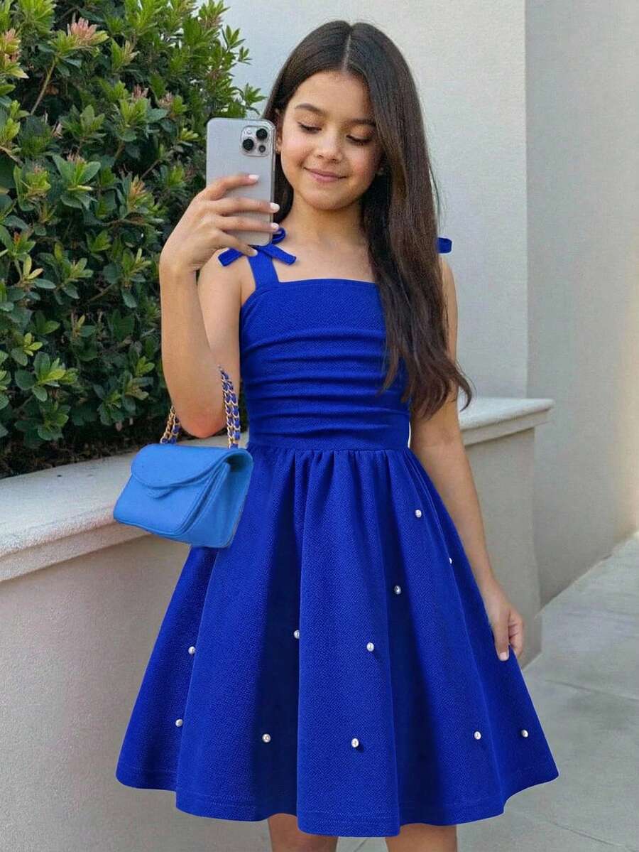Tween girl wearing a purple sleeveless striped cami mini dress featuring a high waist flared hem and beaded pearl details.