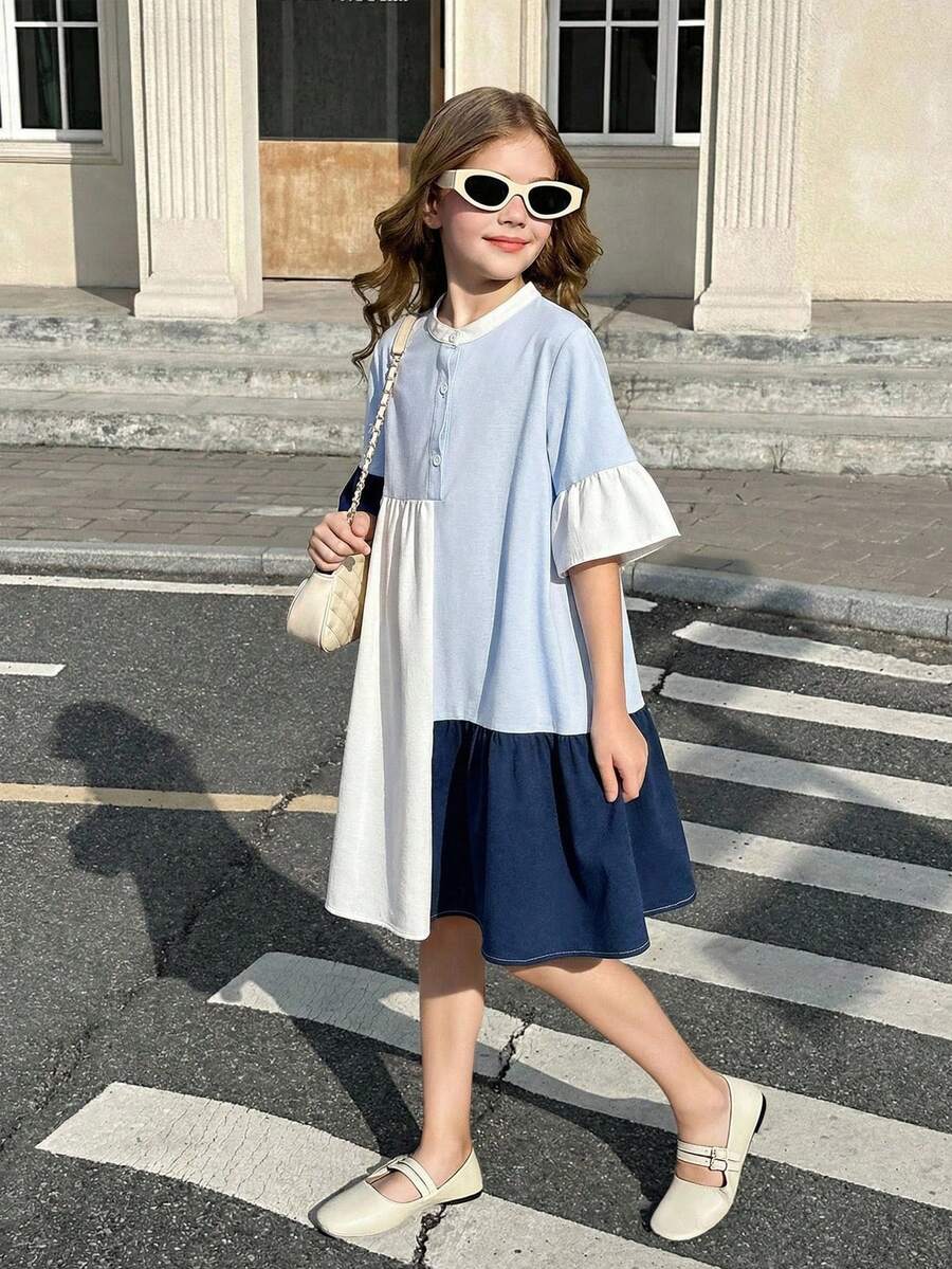 Tween girl wearing a black striped smock shirt dress with flounce half sleeves, a stand collar, and a ruffled hem.