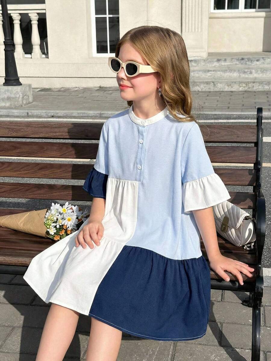 Tween girl wearing a black striped smock shirt dress with flounce half sleeves, a stand collar, and a ruffled hem.