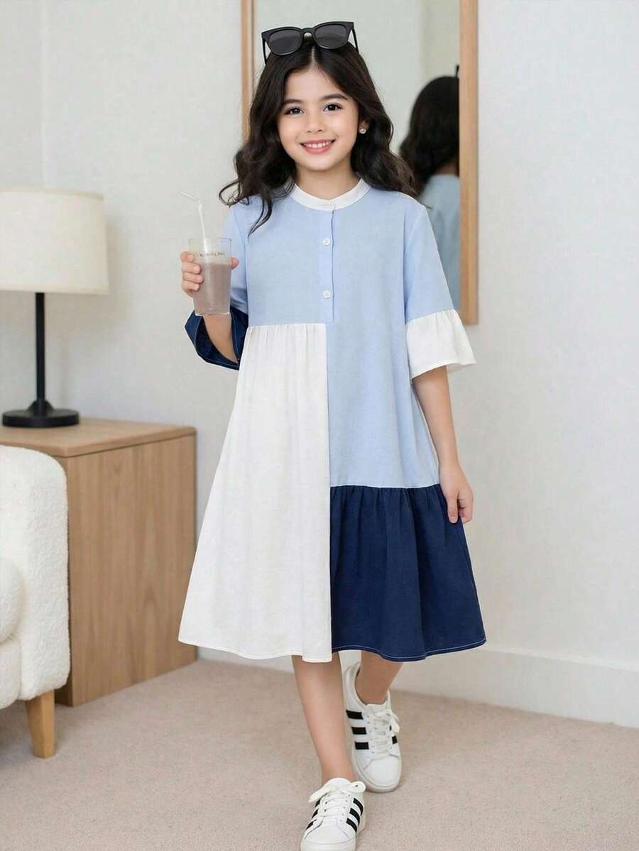 Tween girl wearing a black striped smock shirt dress with flounce half sleeves, a stand collar, and a ruffled hem.