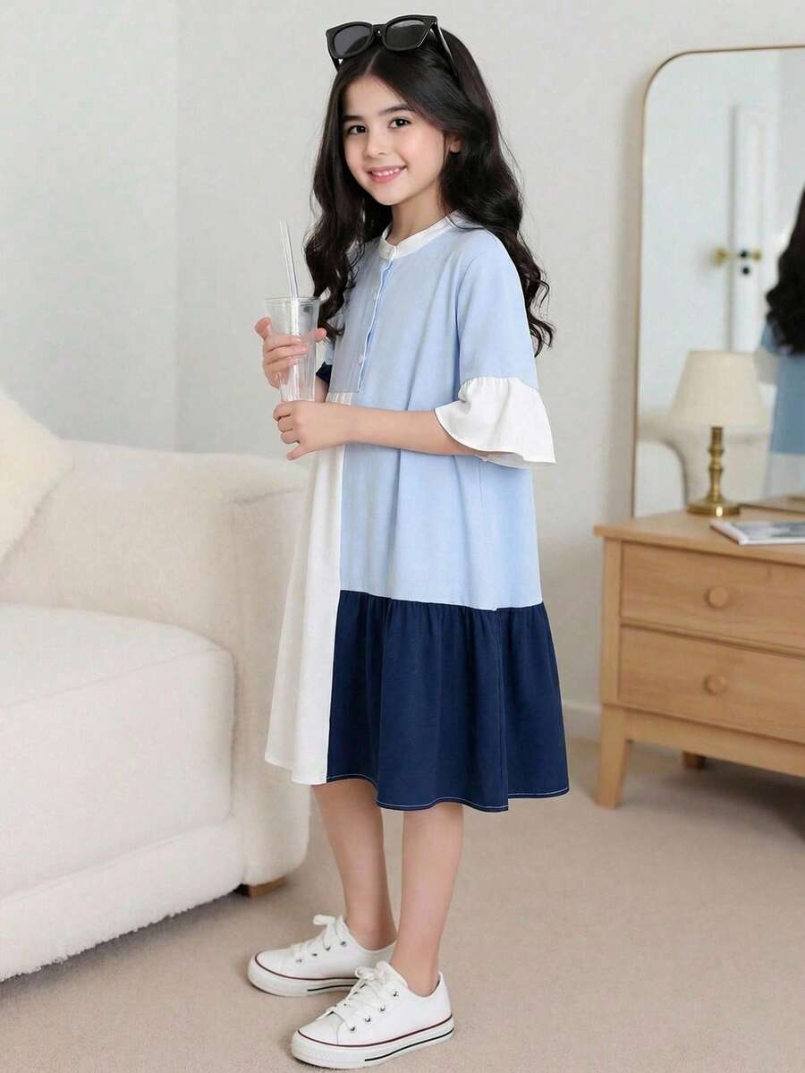 Tween girl wearing a black striped smock shirt dress with flounce half sleeves, a stand collar, and a ruffled hem.
