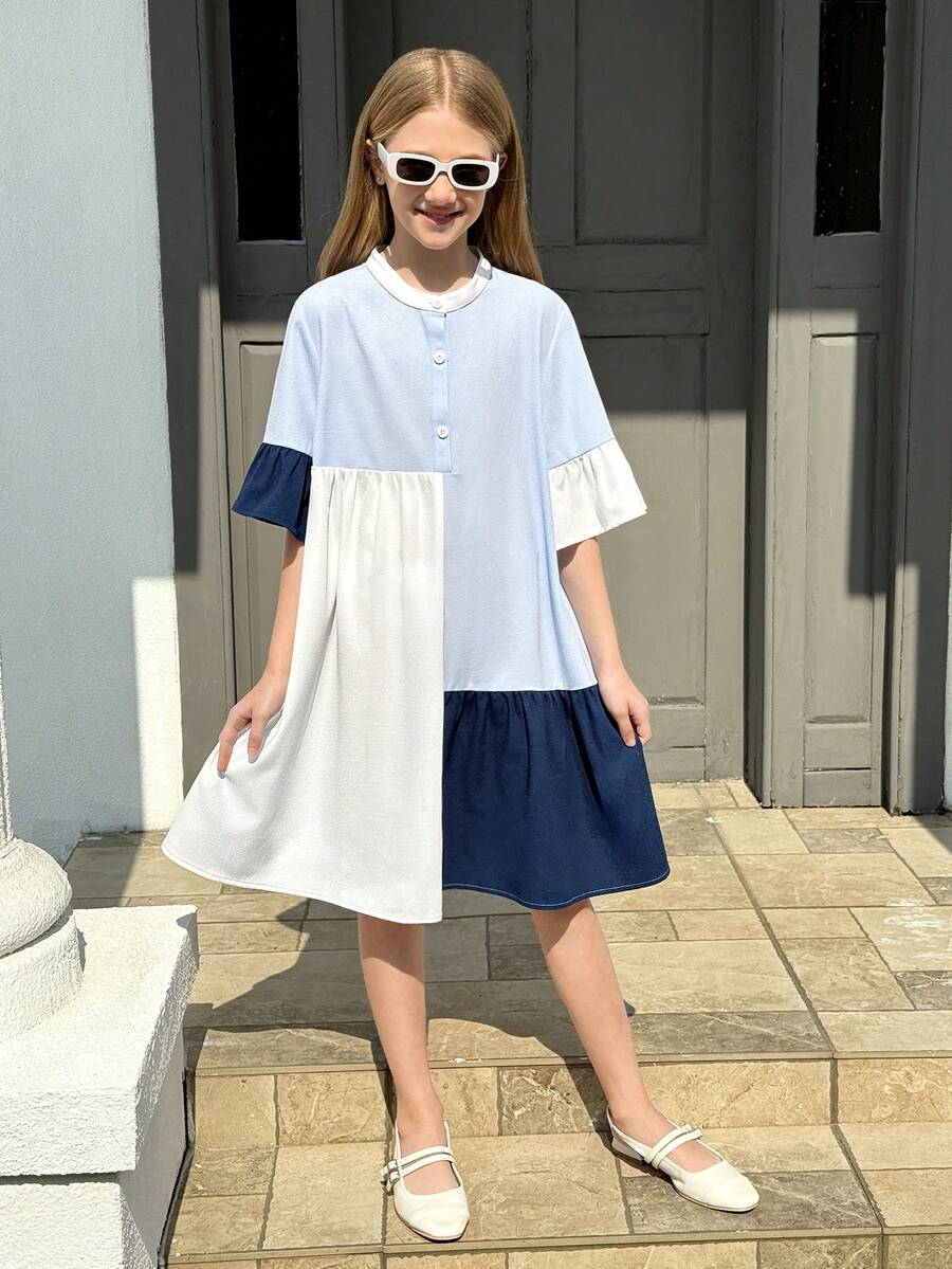 Tween girl wearing a black striped smock shirt dress with flounce half sleeves, a stand collar, and a ruffled hem.