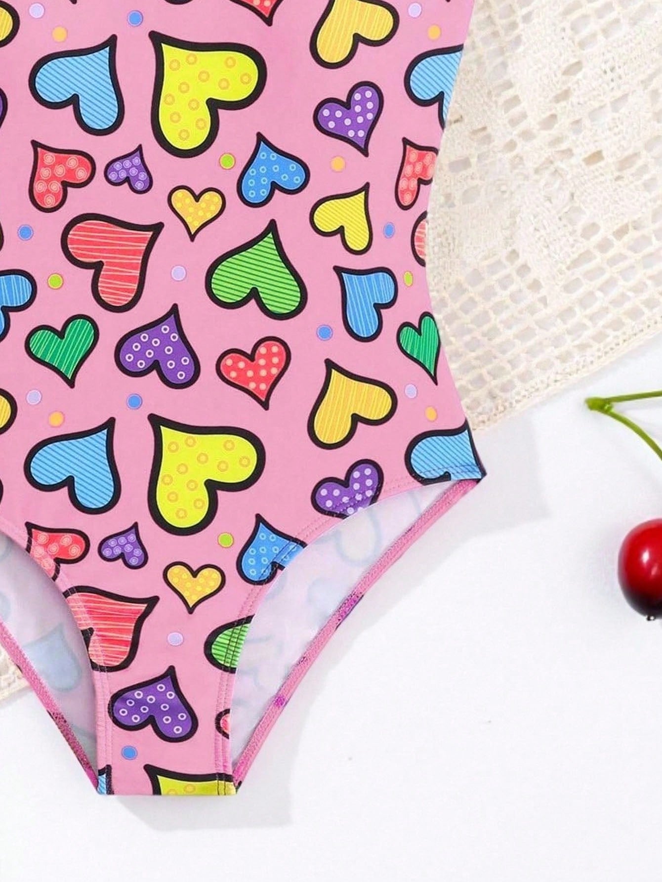 Baby pink girls one-piece swimsuit with ruffle detail, scoop neck, all-over print, and medium-stretch fabric for kids' beach and pool wear.