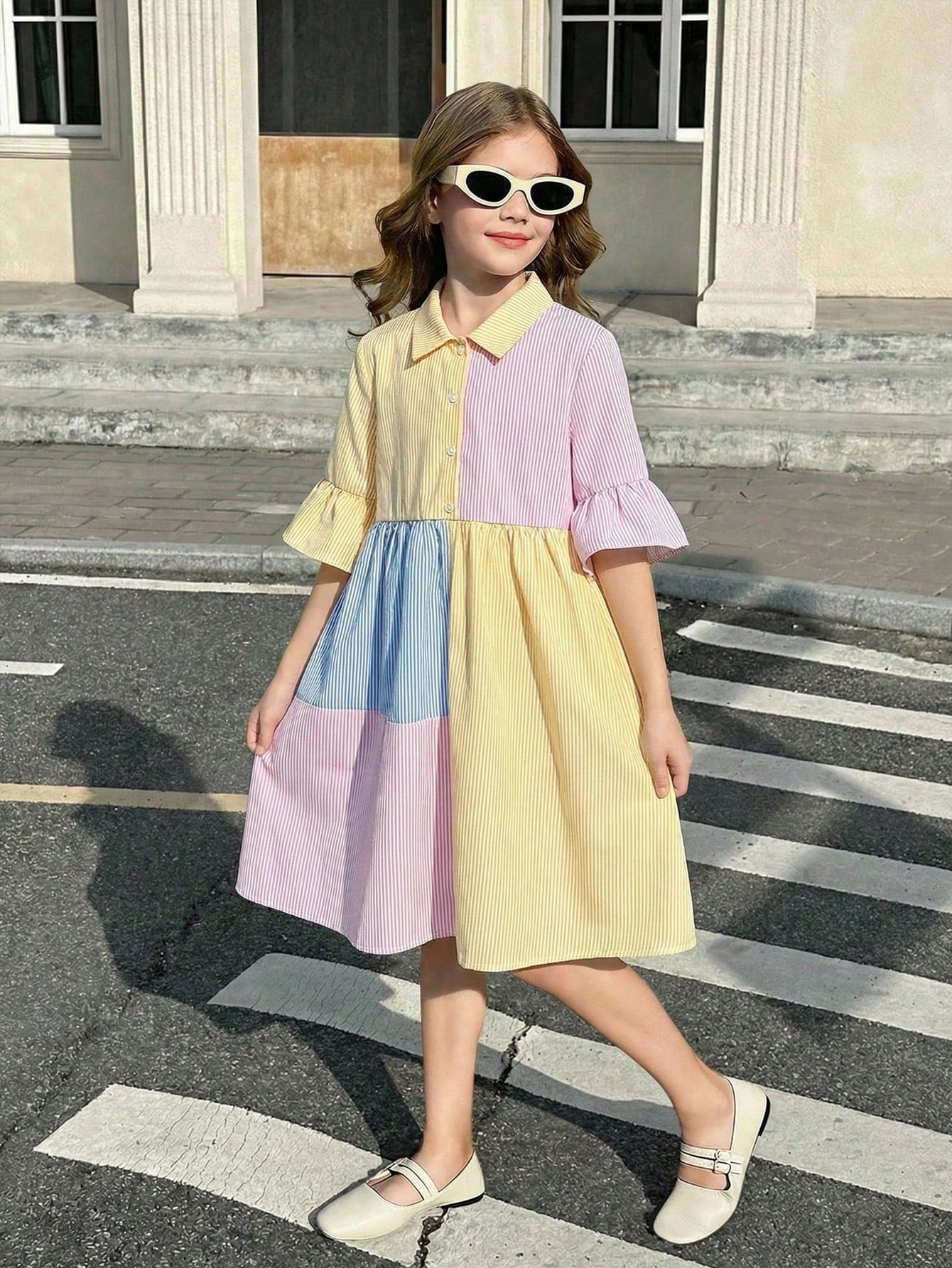 Tween girl wearing a black striped smock shirt dress with flounce half sleeves, a stand collar, and a ruffled hem.