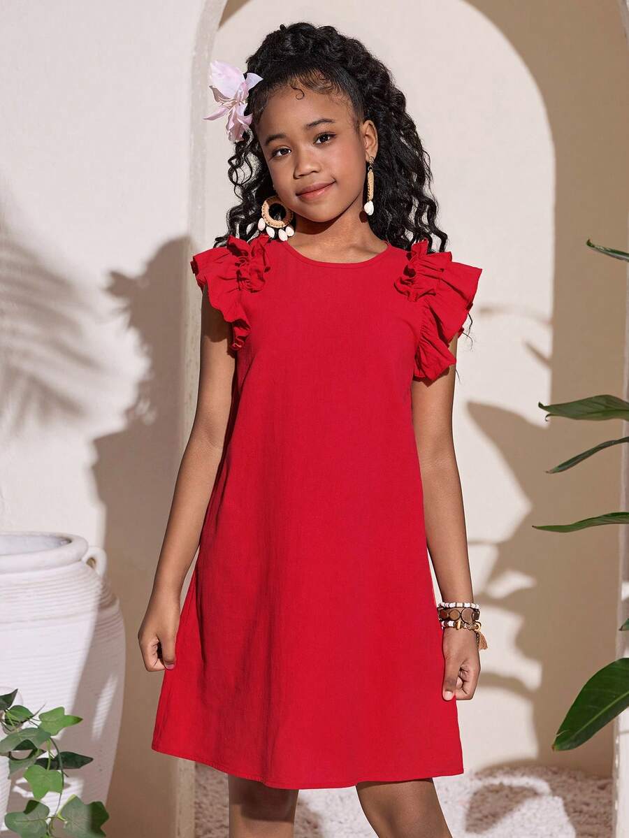 Tween girl wearing a blue ditsy floral patchwork tunic dress with ruffle button details and a round neckline.