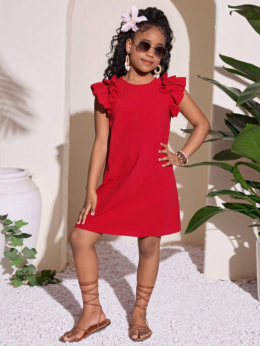 Tween girl wearing a blue ditsy floral patchwork tunic dress with ruffle button details and a round neckline.