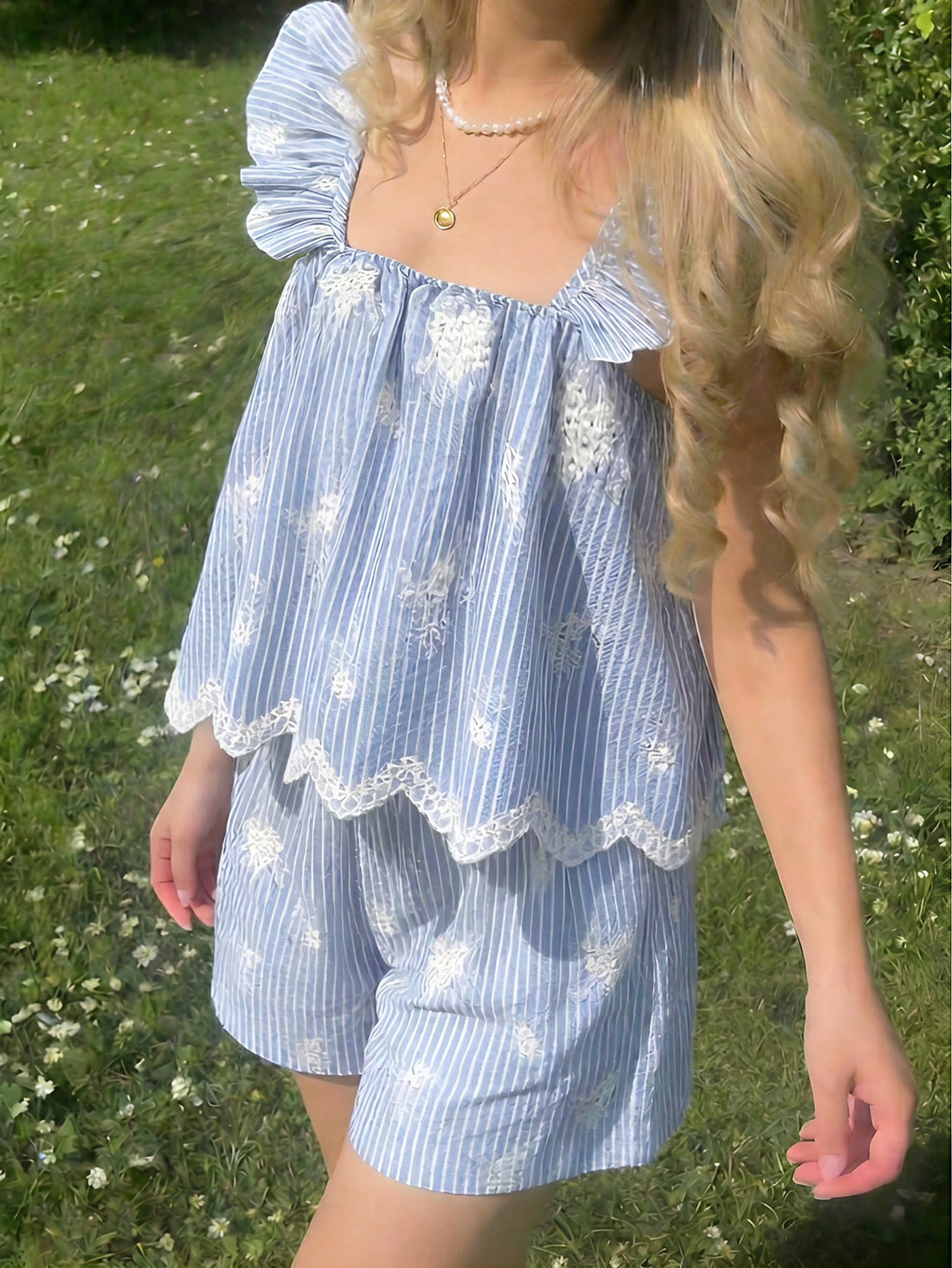 Tween girl wearing a blue and white striped sleeveless top featuring embroidery details and ruffle trim with matching shorts.