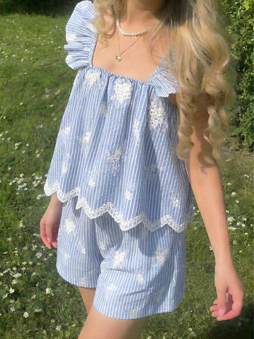 Tween girl wearing a blue and white striped sleeveless top featuring embroidery details and ruffle trim with matching shorts.