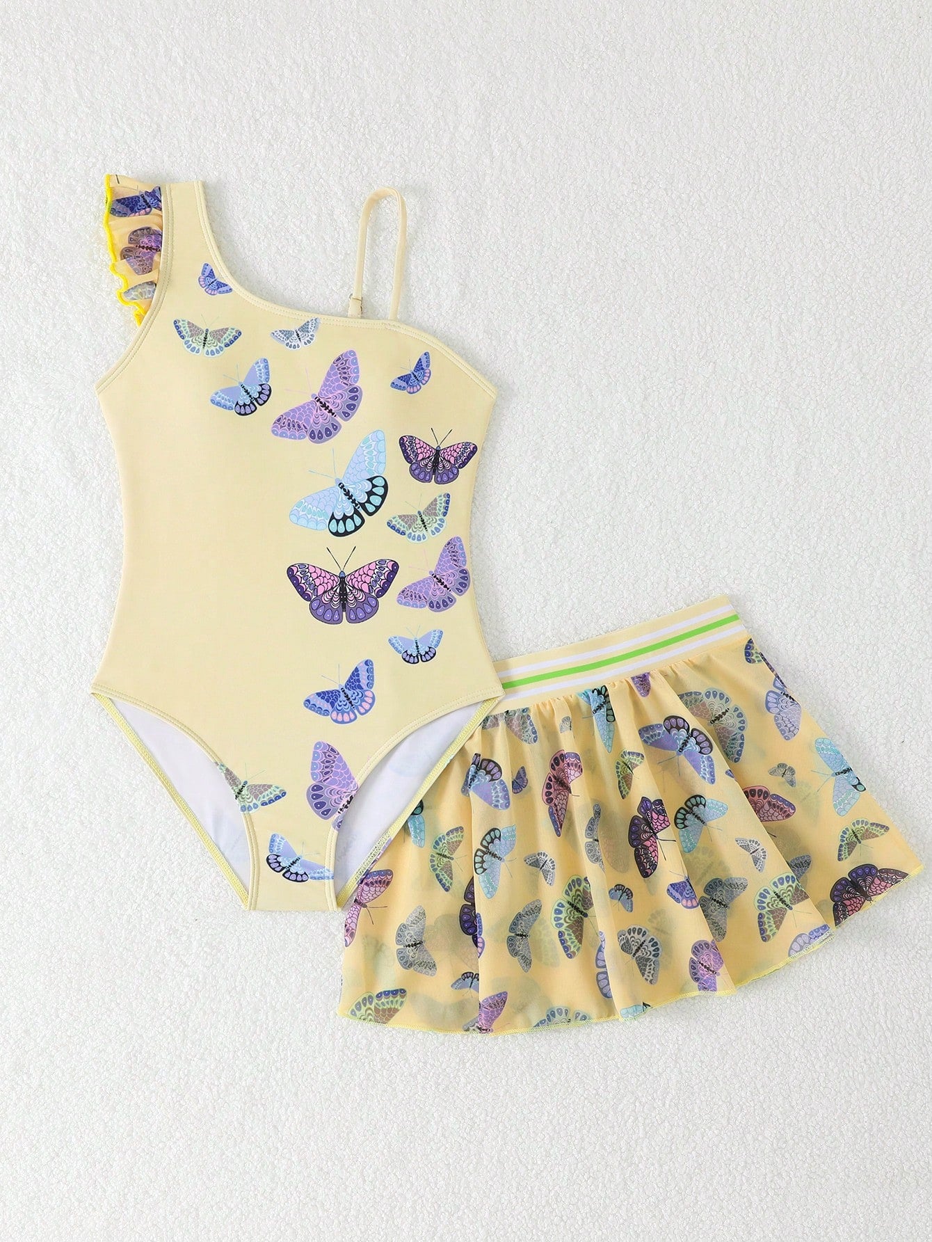 Girls yellow one-piece swimsuit with asymmetrical neckline, ruffle detail, sleeveless fitted style, and skirt bottom for beach and pool vacations.