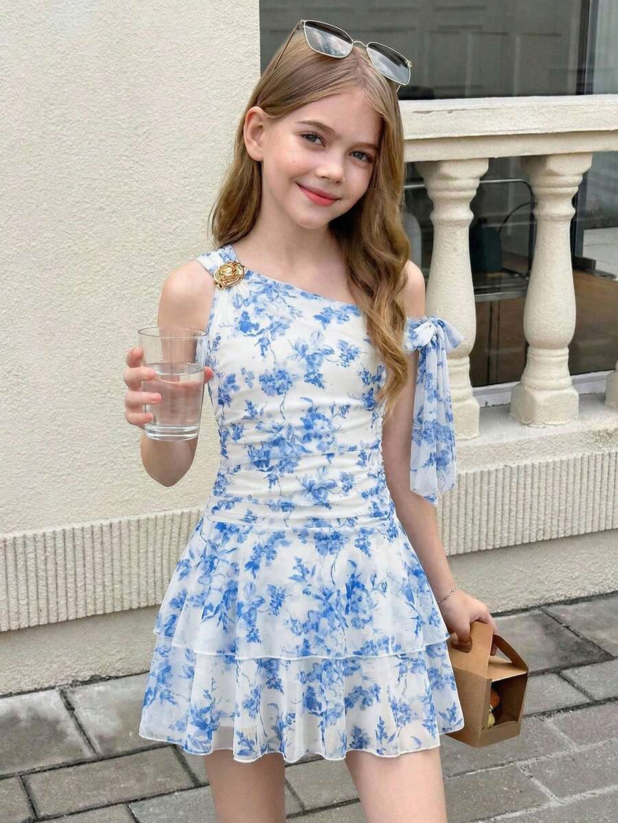 Tween girl wearing an apricot asymmetrical tiered sleeveless party dress with an A-line silhouette.