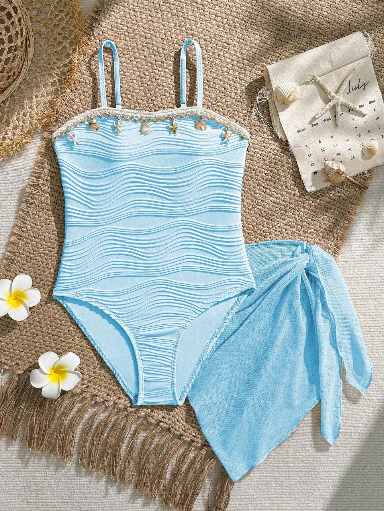 Blue girls one-piece swimsuit with spaghetti straps, textured plain fabric, shell-inspired detail, and matching skirt bottom for beach or pool vacation wear.