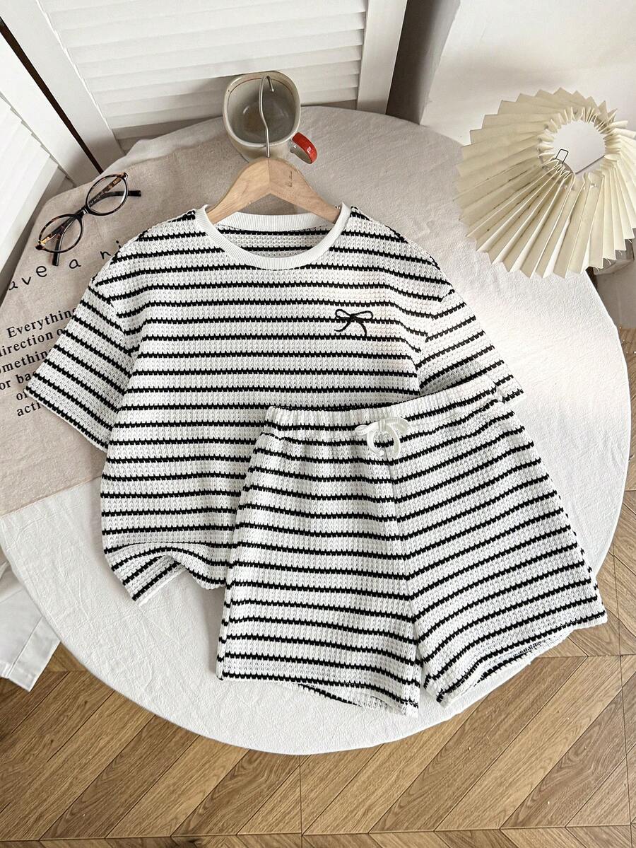 Tween girl wearing a black and white striped drop-shoulder crew neck t-shirt with bow embroidery paired with matching tie-waist shorts.