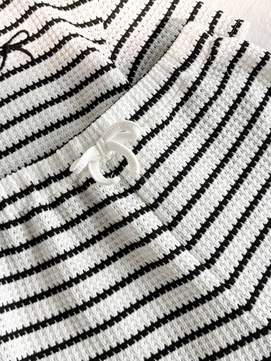 Tween girl wearing a black and white striped drop-shoulder crew neck t-shirt with bow embroidery paired with matching tie-waist shorts.