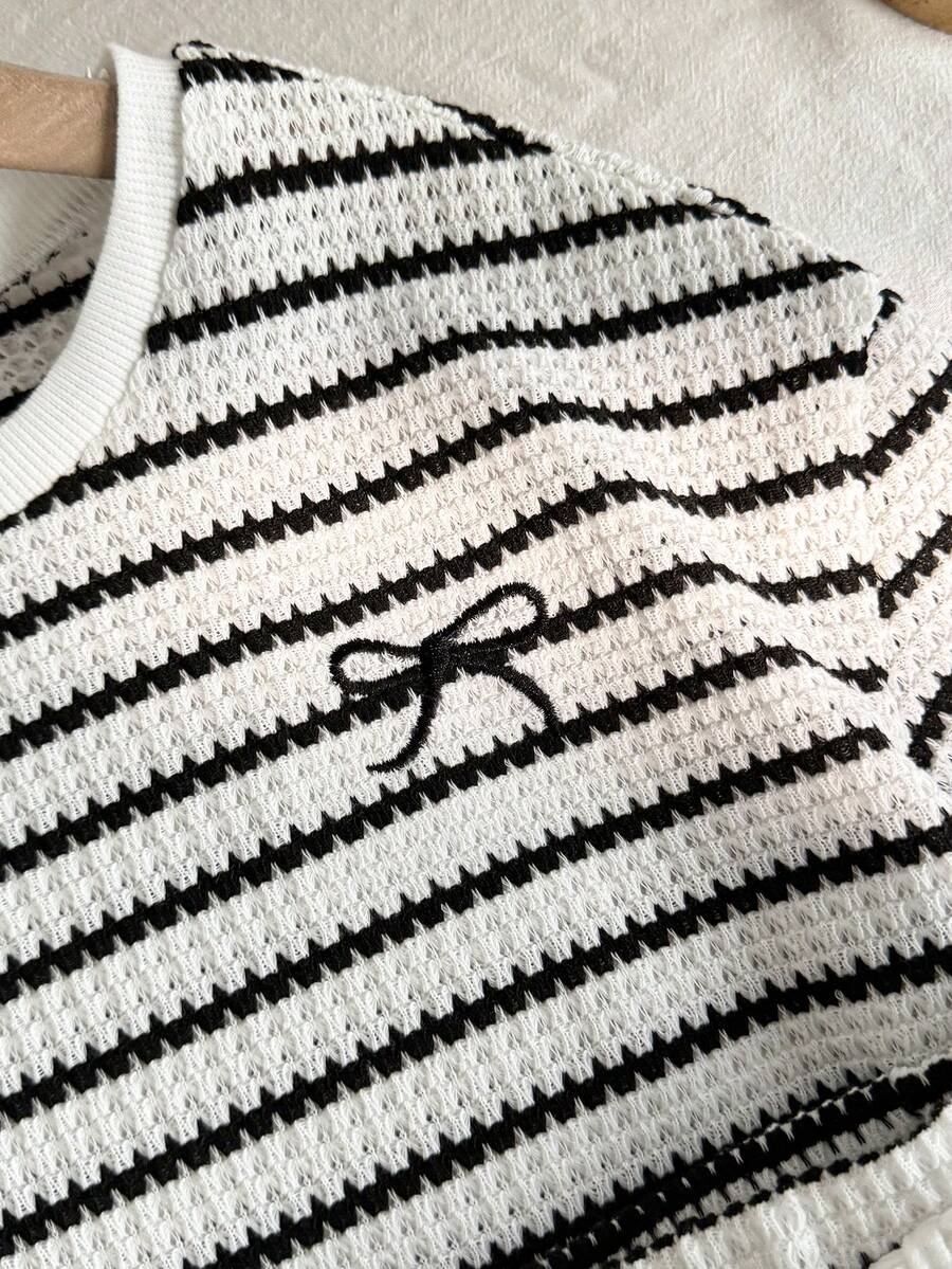 Tween girl wearing a black and white striped drop-shoulder crew neck t-shirt with bow embroidery paired with matching tie-waist shorts.
