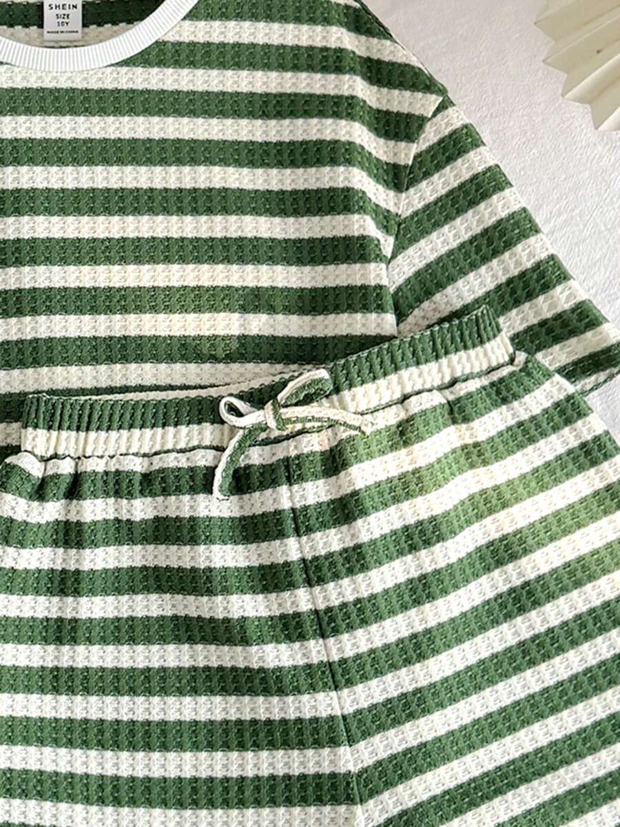 Tween girl wearing a black and white striped drop-shoulder crew neck t-shirt with bow embroidery paired with matching tie-waist shorts.