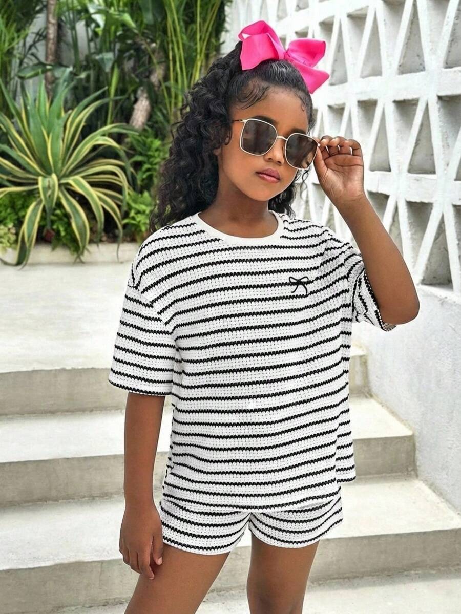 Tween girl wearing a black and white striped drop-shoulder crew neck t-shirt with bow embroidery paired with matching tie-waist shorts.
