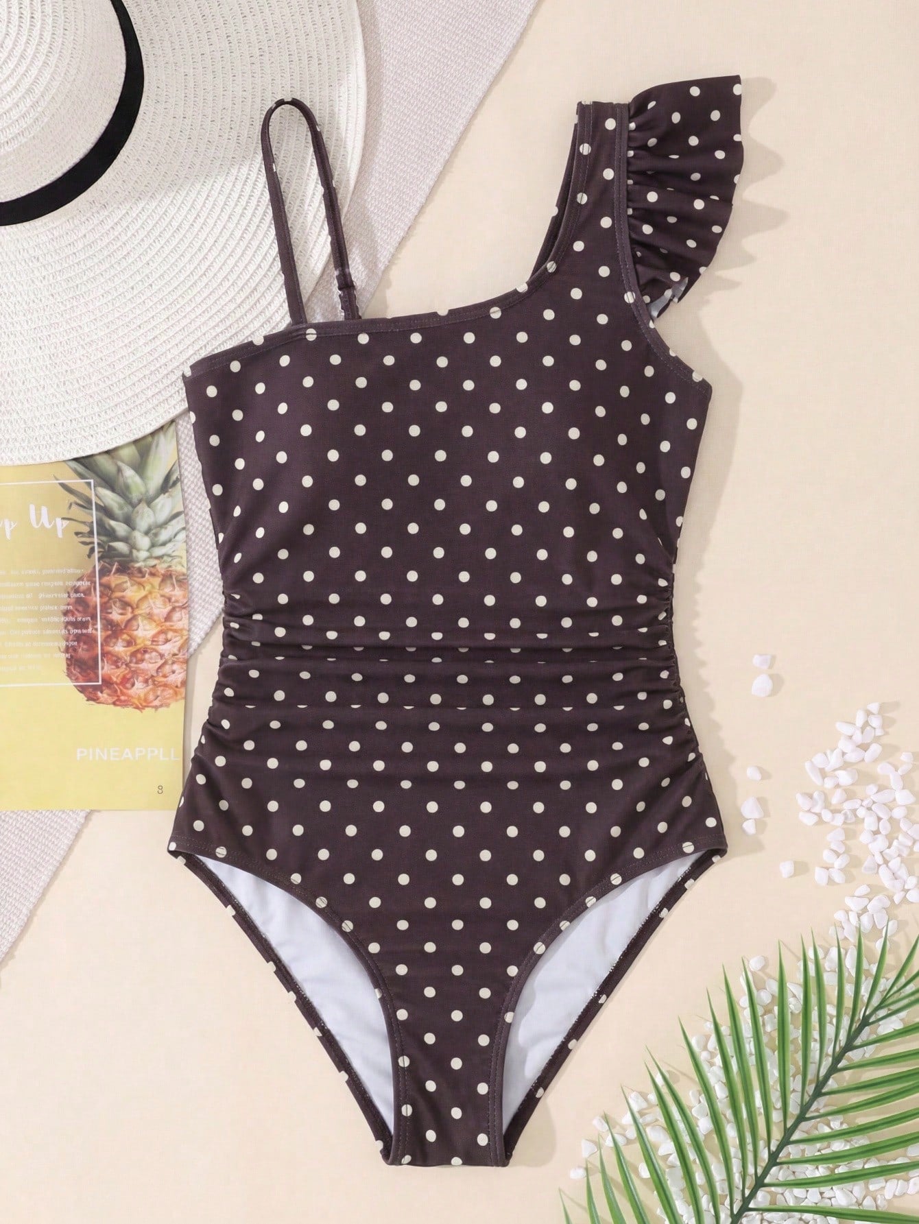 Tween girl one-piece swimsuit in brown polka dot geometric print with asymmetrical neckline, ruffle detail, cut-out design, and fitted mid-waist swim bottom.