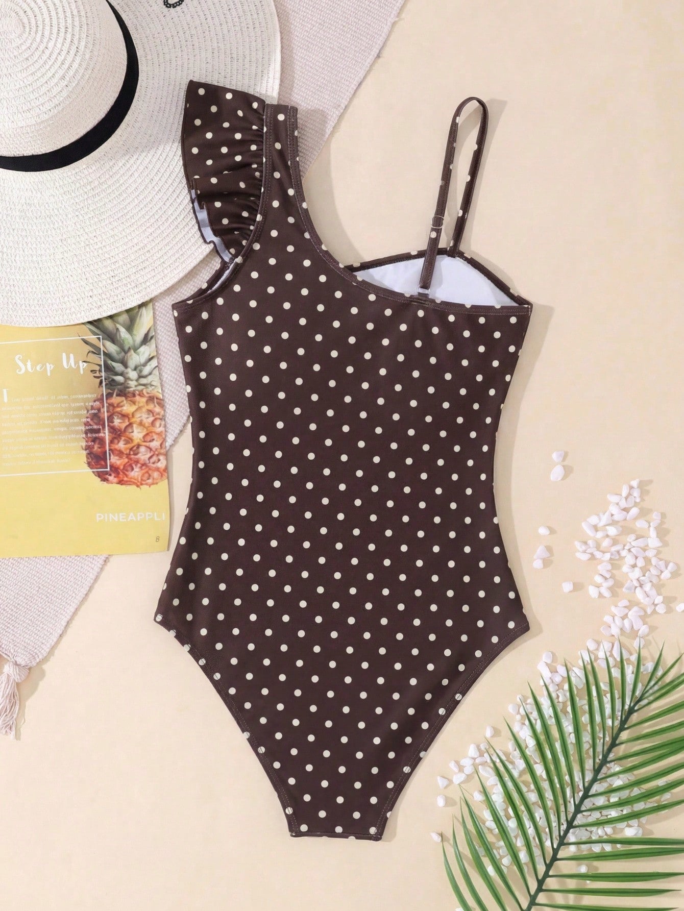Tween girl one-piece swimsuit in brown polka dot geometric print with asymmetrical neckline, ruffle detail, cut-out design, and fitted mid-waist swim bottom.