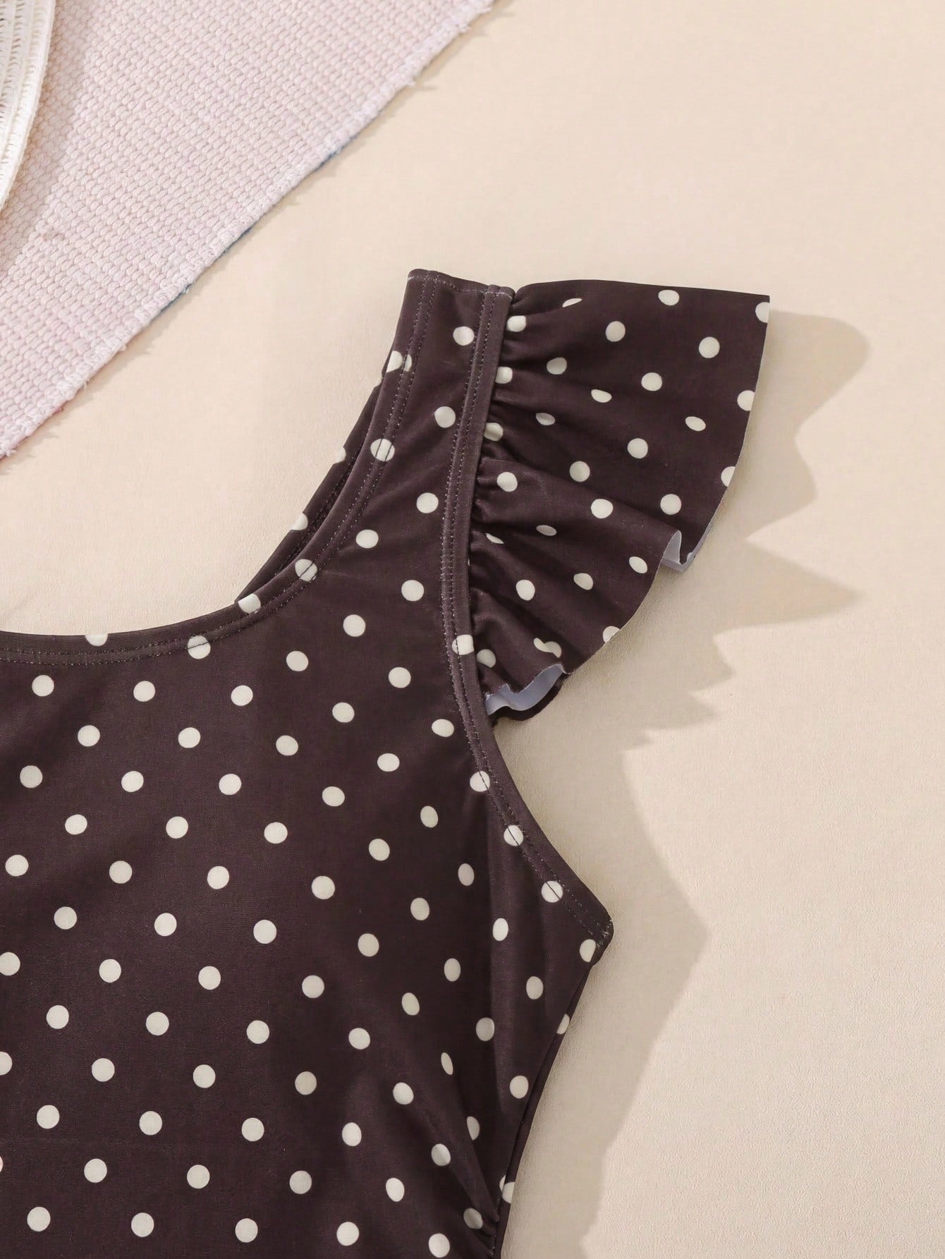 Tween girl one-piece swimsuit in brown polka dot geometric print with asymmetrical neckline, ruffle detail, cut-out design, and fitted mid-waist swim bottom.