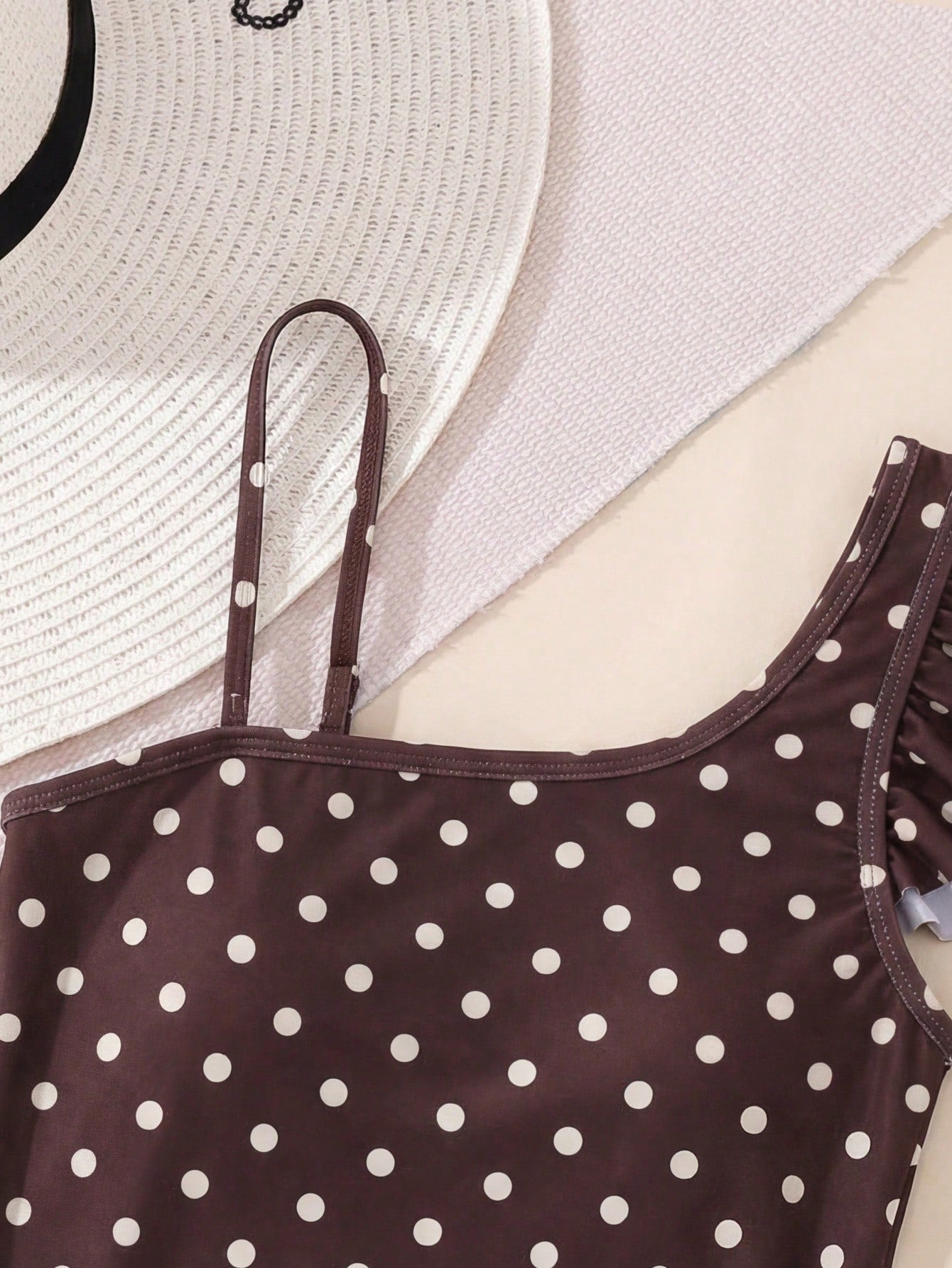 Tween girl one-piece swimsuit in brown polka dot geometric print with asymmetrical neckline, ruffle detail, cut-out design, and fitted mid-waist swim bottom.