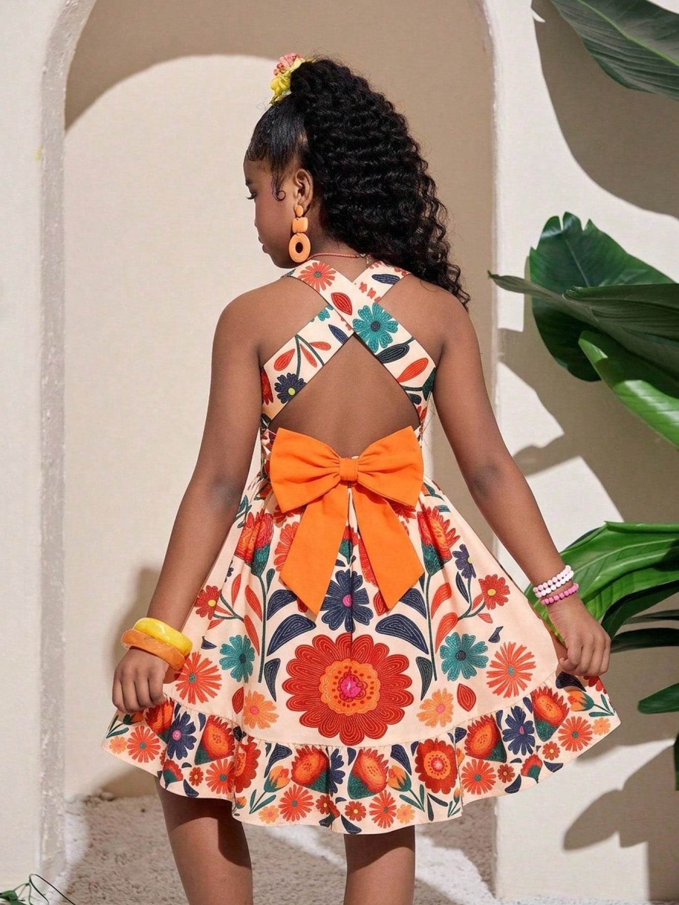 Pink sleeveless tween girls vacation dress with all-over fruit and vegetable print, strap neckline, belted high waist, cut-out detail, and flared ruffle hem.