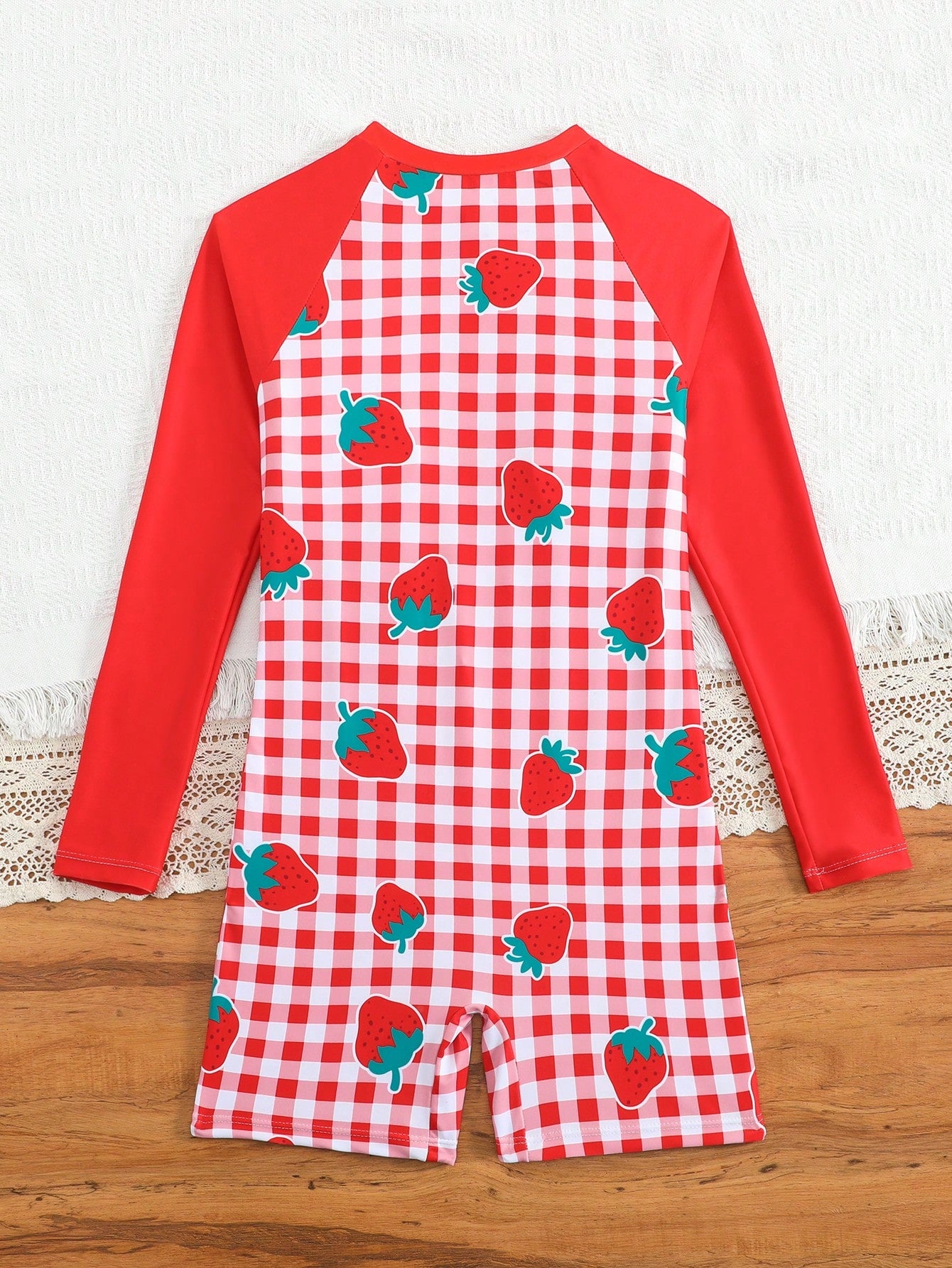 Tween girls one-piece swimsuit featuring a high neck, long sleeves, and shorts bottom, with a back zipper and strawberry plaid digital print on stretch knit fabric. Designed for swimming, vacation, and summer wear.