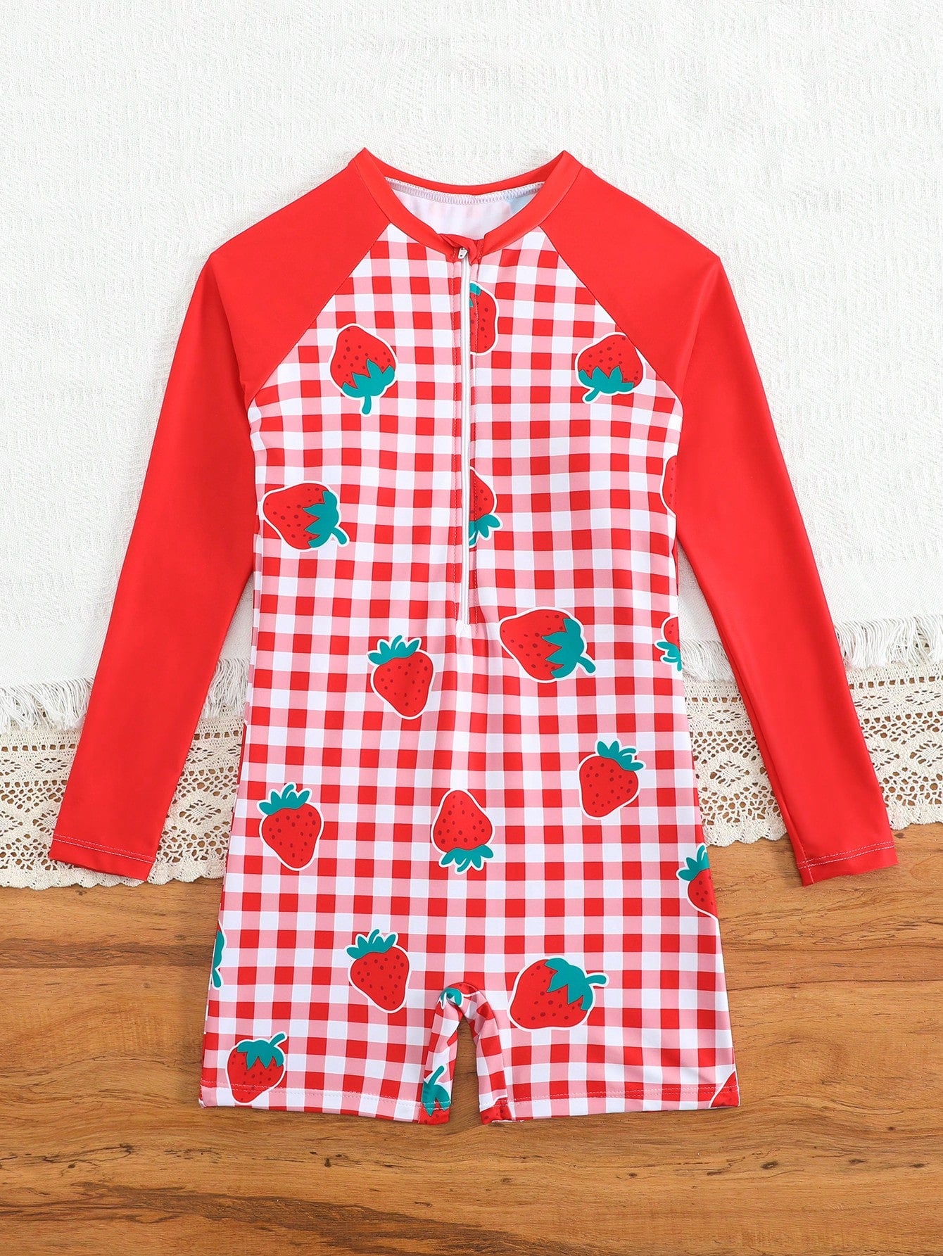Tween girls one-piece swimsuit featuring a high neck, long sleeves, and shorts bottom, with a back zipper and strawberry plaid digital print on stretch knit fabric. Designed for swimming, vacation, and summer wear.