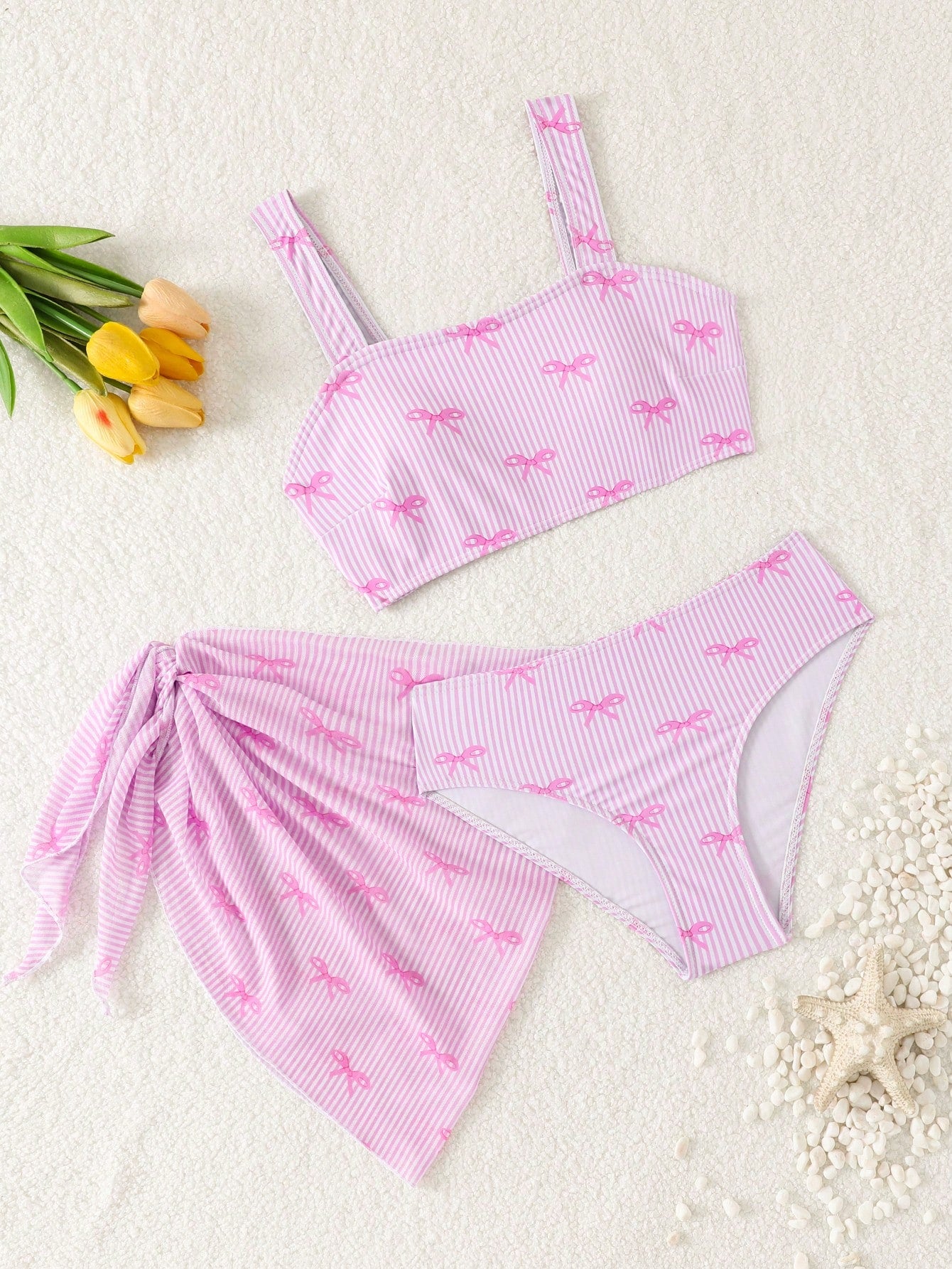 Tween girls three-piece bikini set featuring a bow print bandeau-style top, matching mid-waist bikini bottom, and a sheer mesh cover skirt in a cute beachwear style.