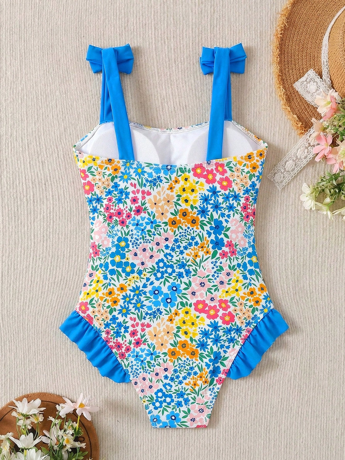 Girls' multicolor one-piece swimsuit with floral plant print, bow detail, asymmetrical ruffle accent, strap neckline, and lined body for beach vacations.