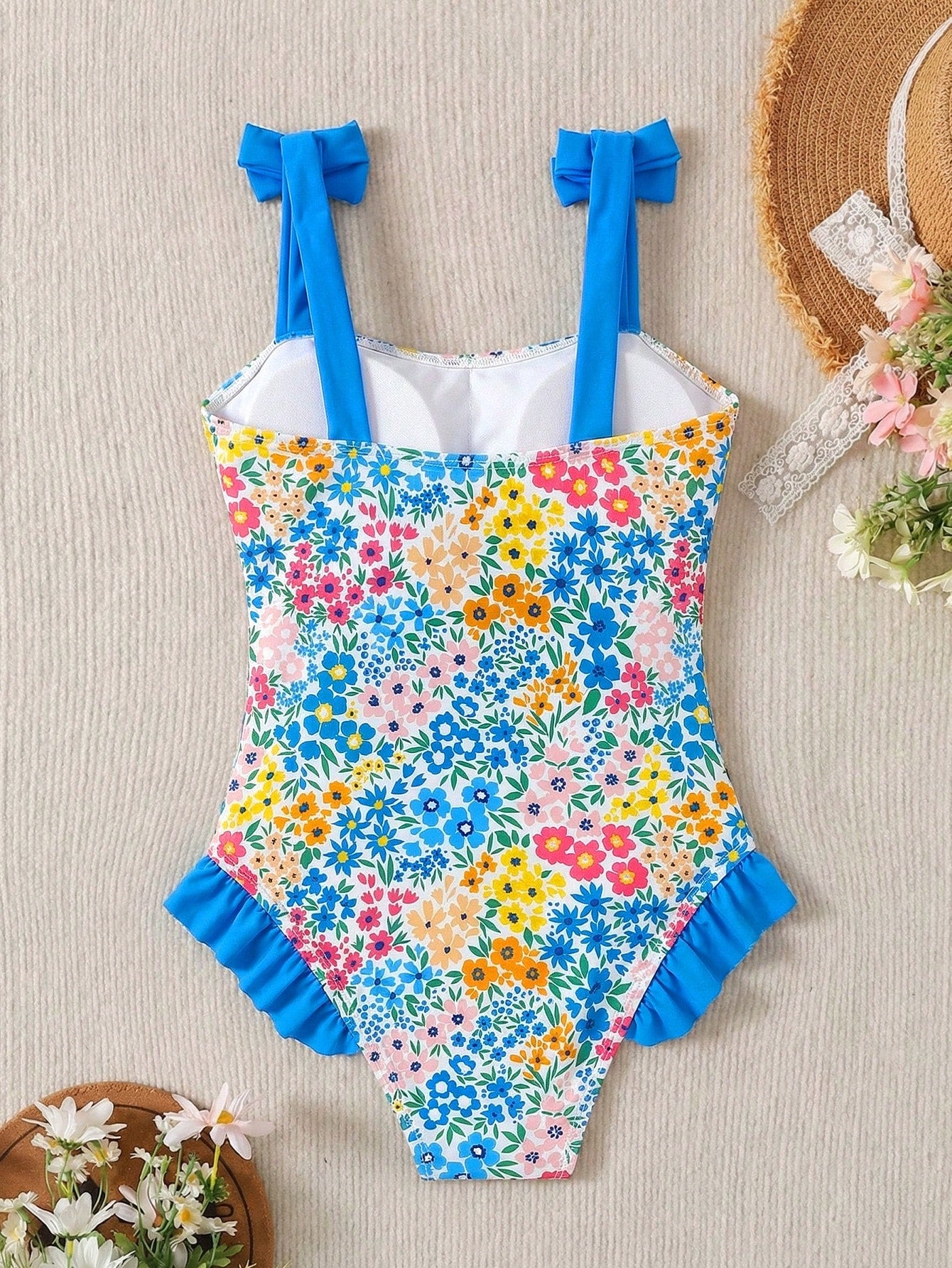 Girls' multicolor one-piece swimsuit with floral plant print, bow detail, asymmetrical ruffle accent, strap neckline, and lined body for beach vacations.