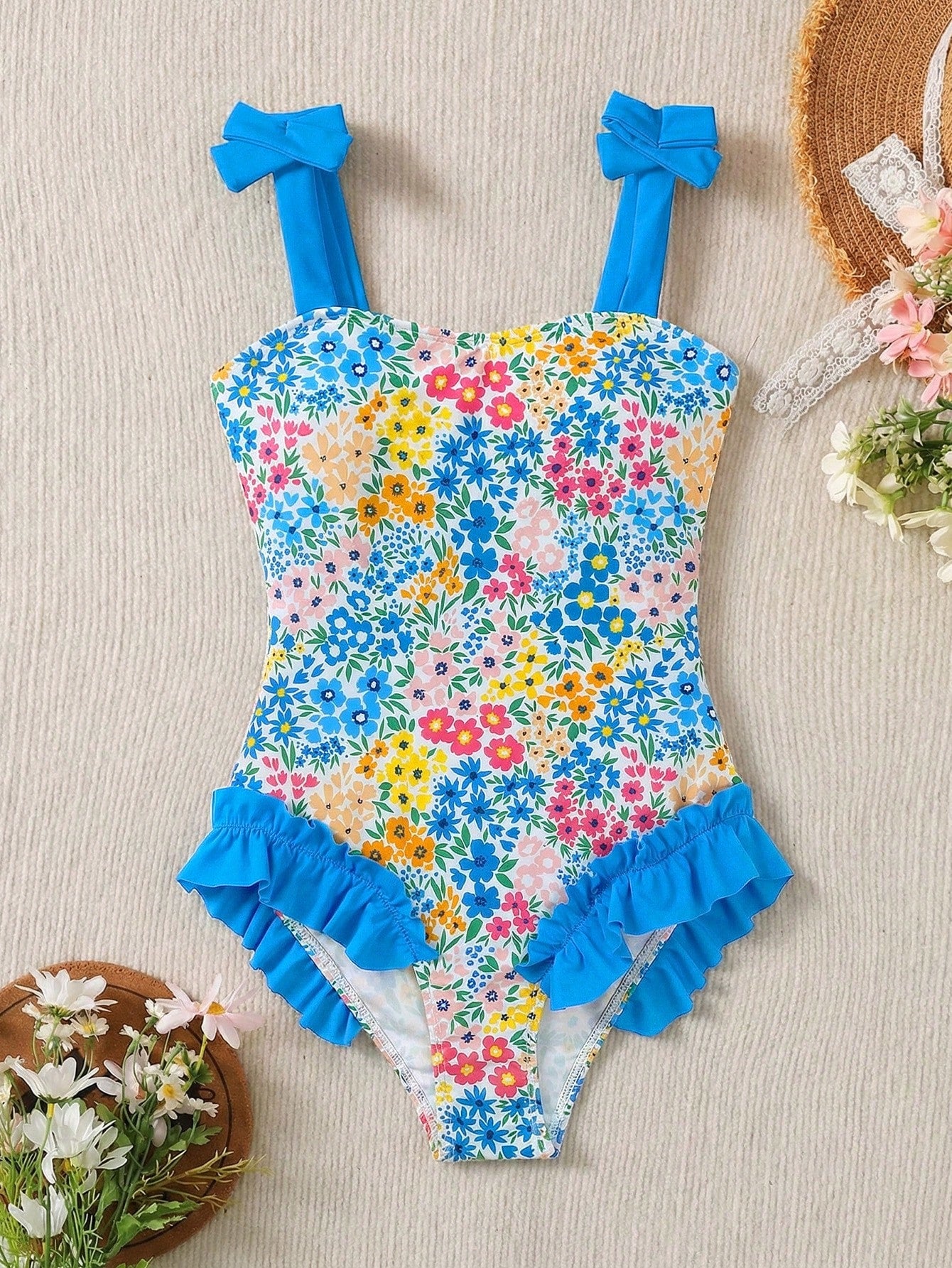 Girls' multicolor one-piece swimsuit with floral plant print, bow detail, asymmetrical ruffle accent, strap neckline, and lined body for beach vacations.