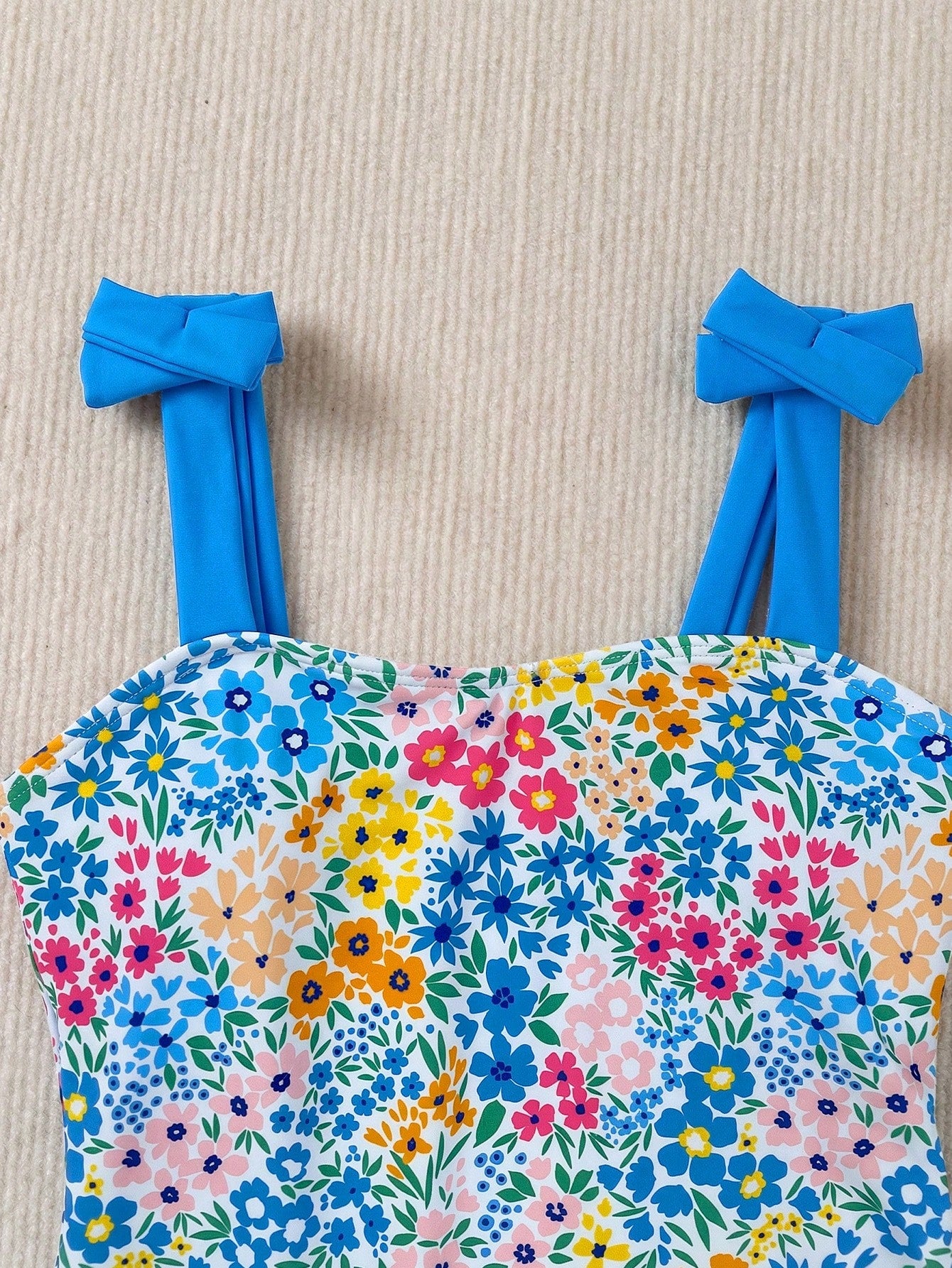 Girls' multicolor one-piece swimsuit with floral plant print, bow detail, asymmetrical ruffle accent, strap neckline, and lined body for beach vacations.
