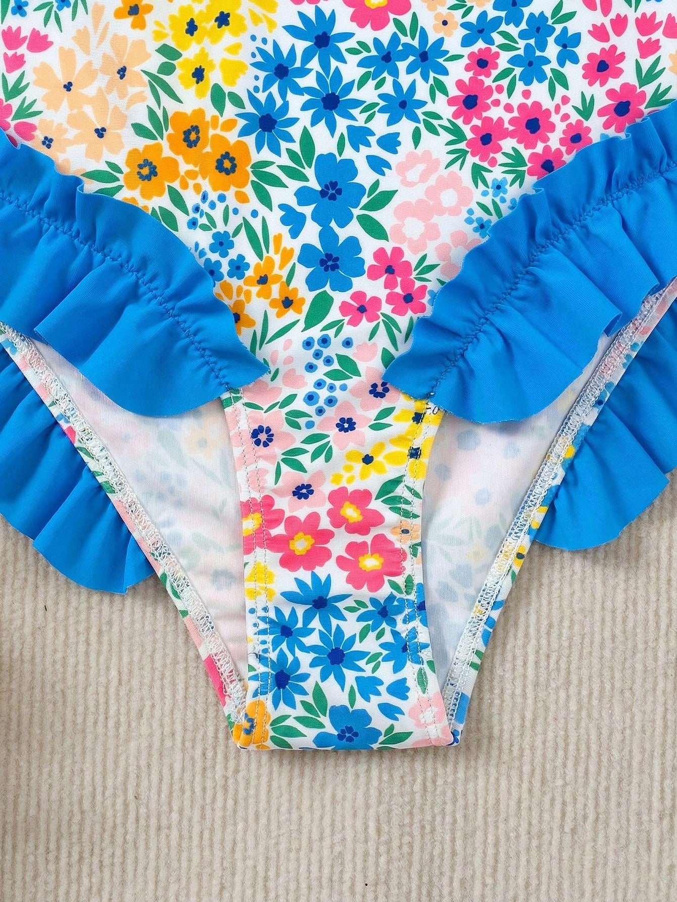 Girls' multicolor one-piece swimsuit with floral plant print, bow detail, asymmetrical ruffle accent, strap neckline, and lined body for beach vacations.
