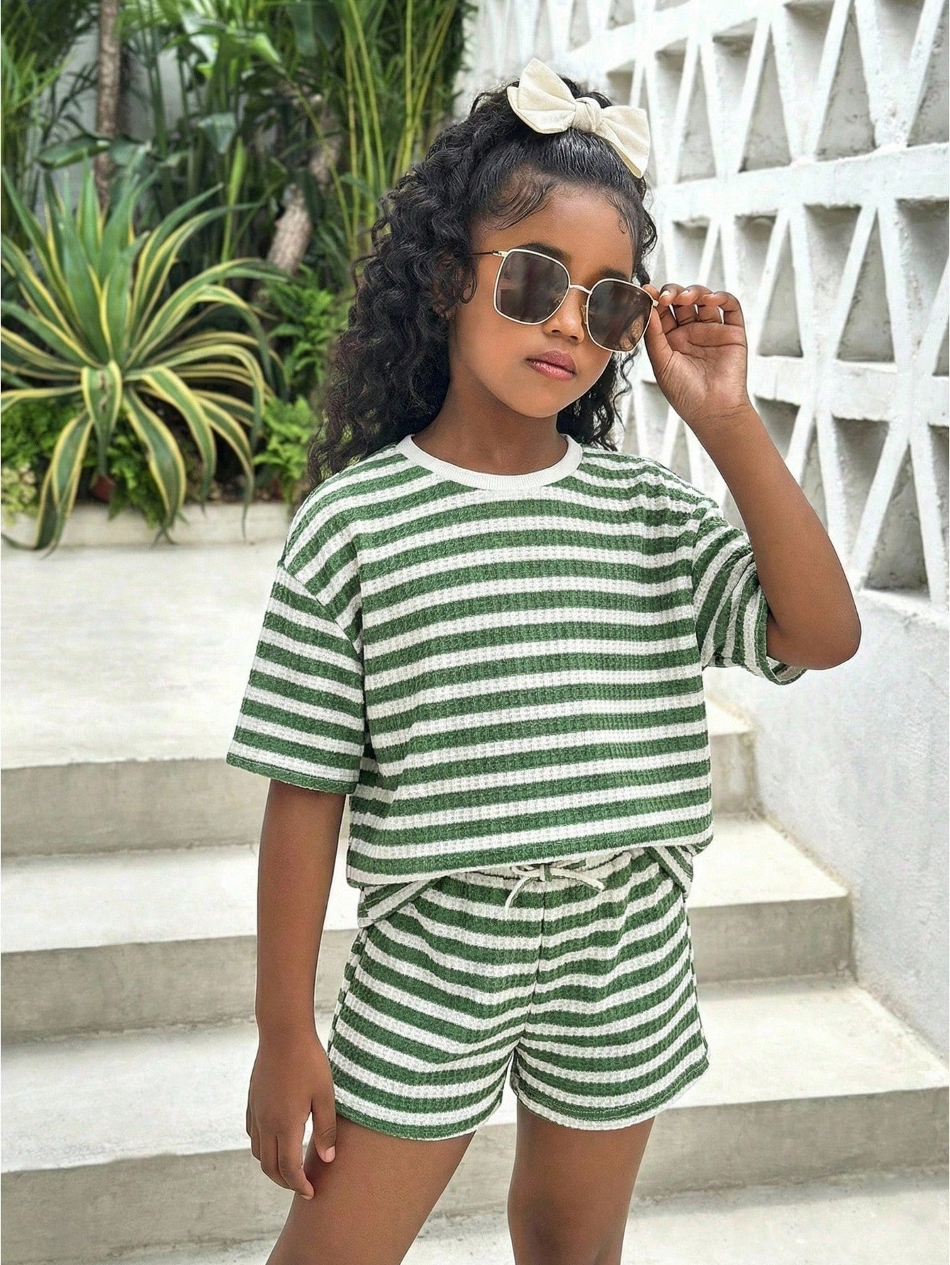 Tween girl wearing a black and white striped drop-shoulder crew neck t-shirt with bow embroidery paired with matching tie-waist shorts.