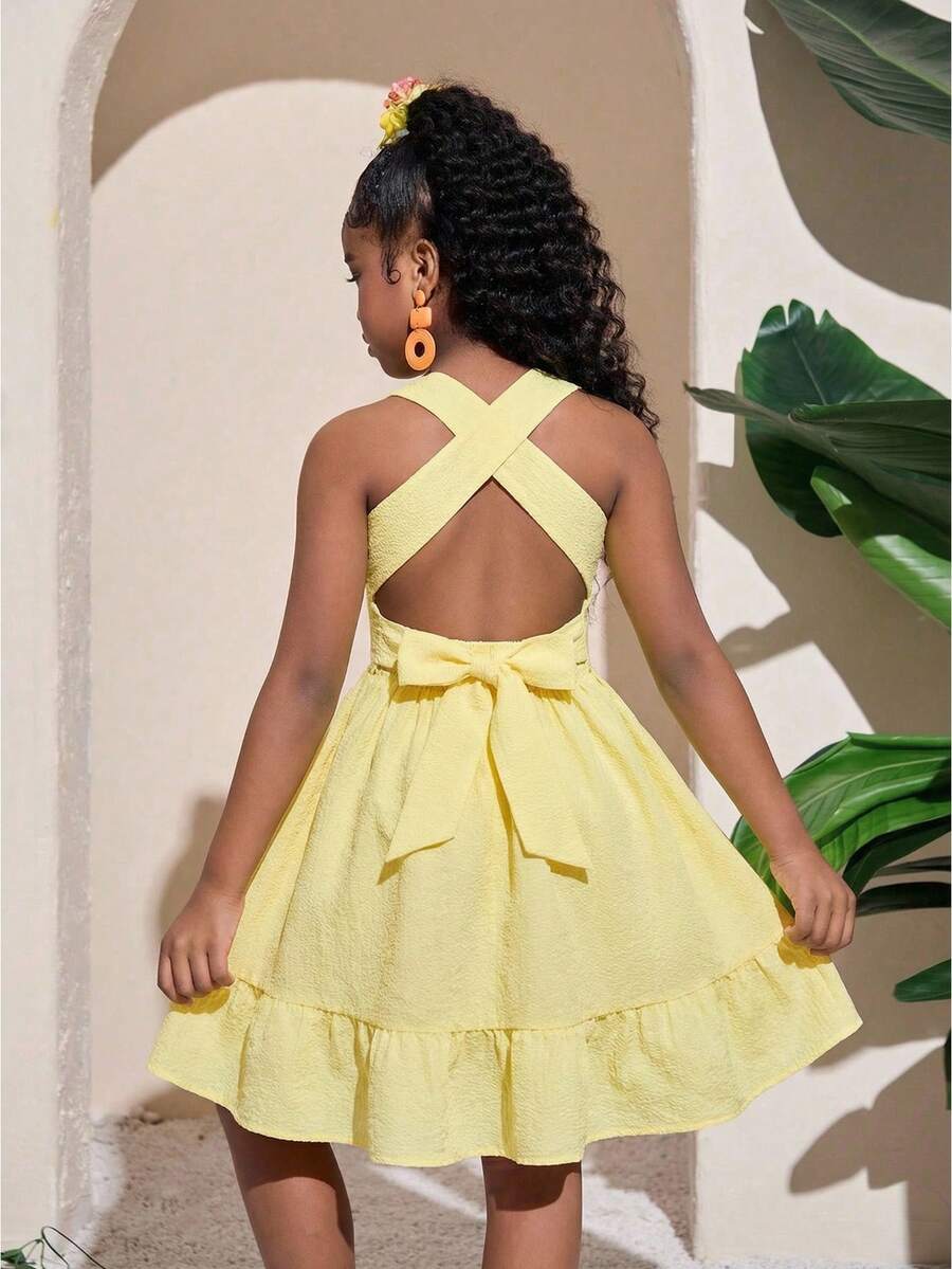 Pink sleeveless tween girls vacation dress with all-over fruit and vegetable print, strap neckline, belted high waist, cut-out detail, and flared ruffle hem.