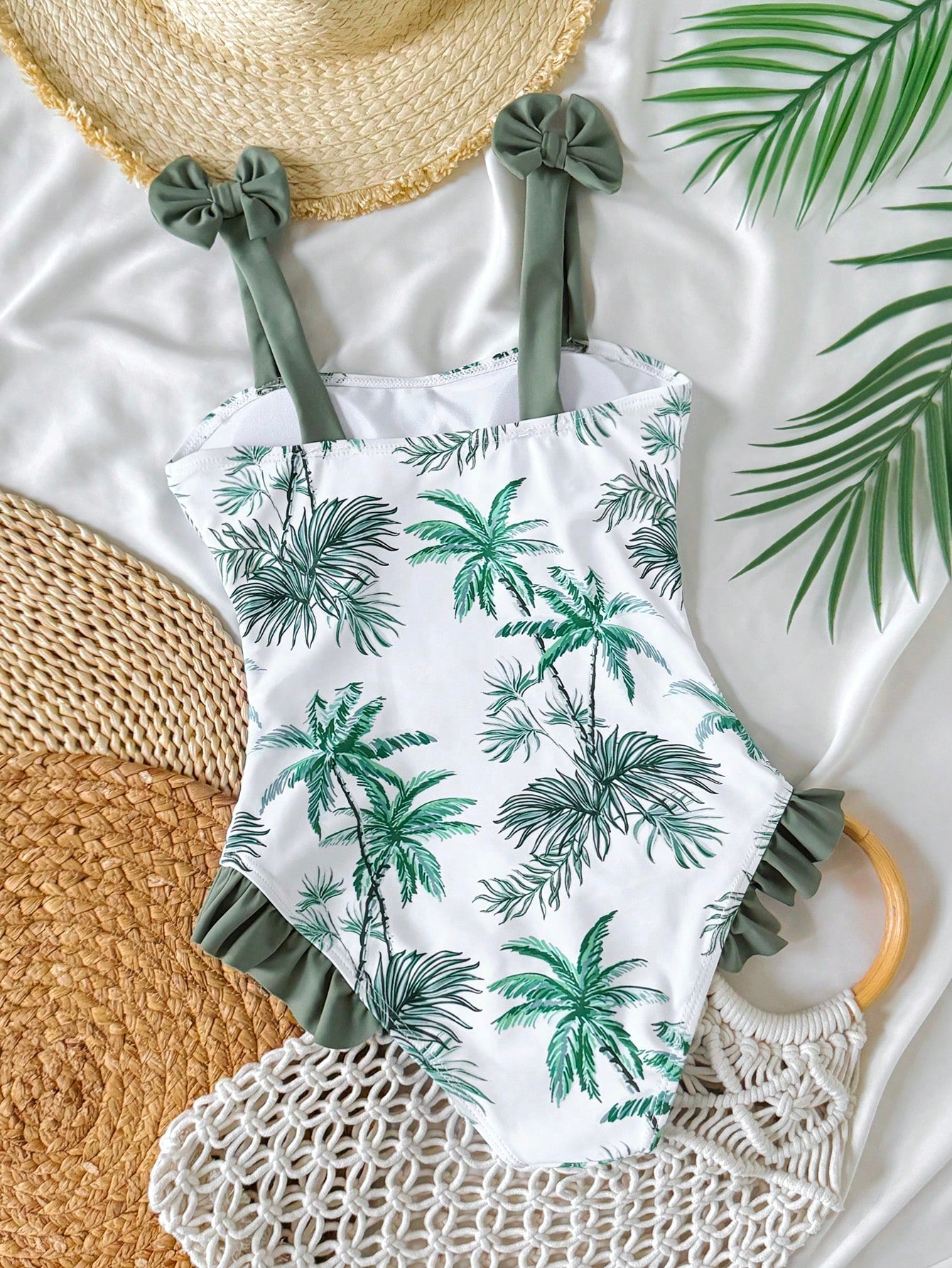 Girls' multicolor one-piece swimsuit with floral plant print, bow detail, asymmetrical ruffle accent, strap neckline, and lined body for beach vacations.