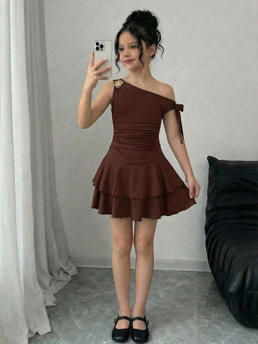 Tween girl wearing an apricot asymmetrical tiered sleeveless party dress with an A-line silhouette.