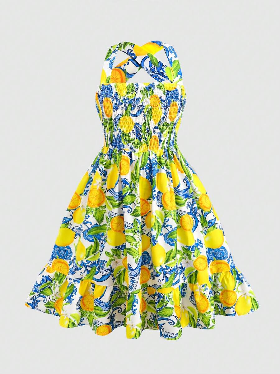 Pink sleeveless tween girls vacation dress with all-over fruit and vegetable print, strap neckline, belted high waist, cut-out detail, and flared ruffle hem.