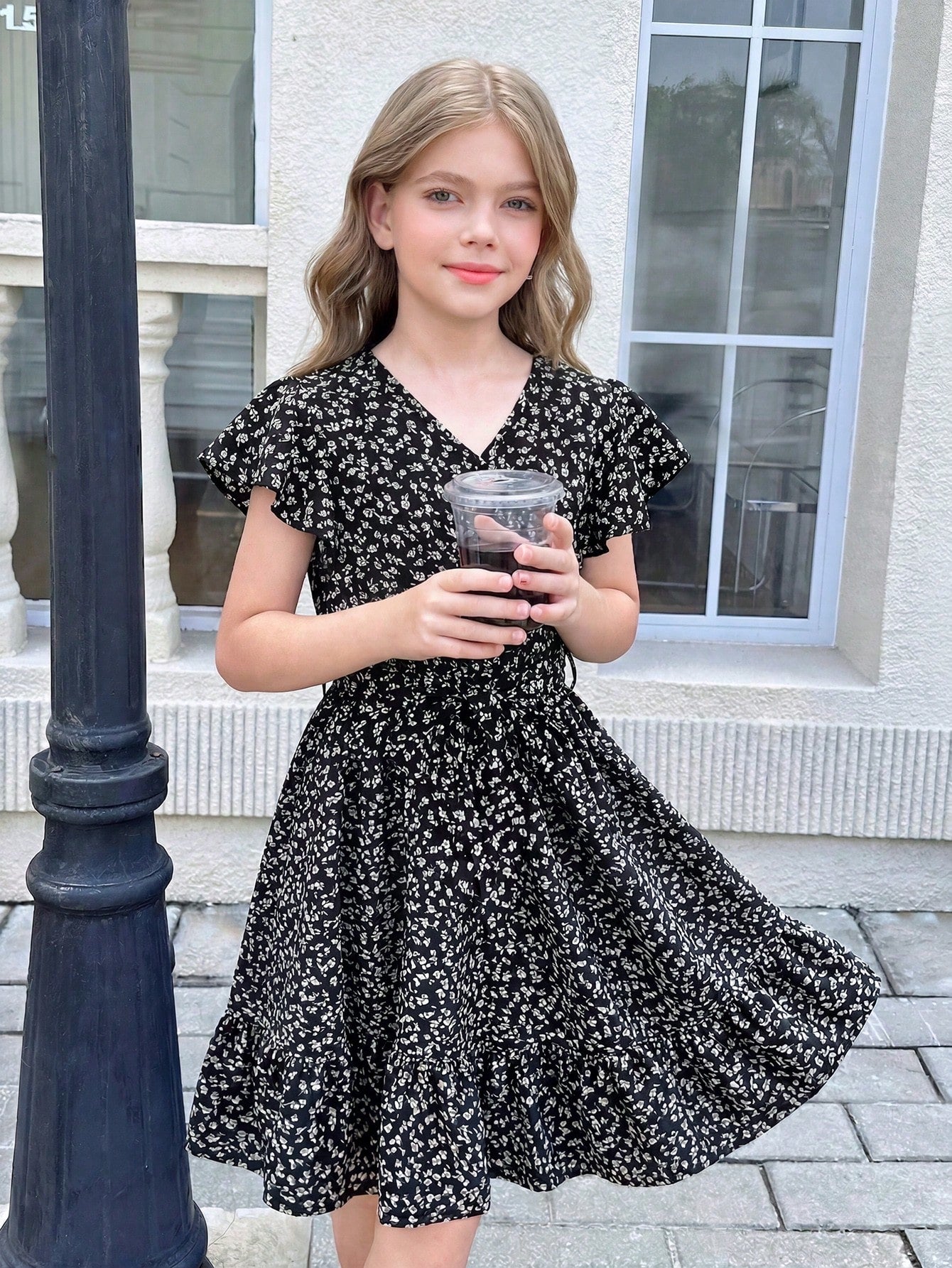 Tween girl wearing a black ditsy floral A-line short dress with V-neckline and flounce short sleeves.