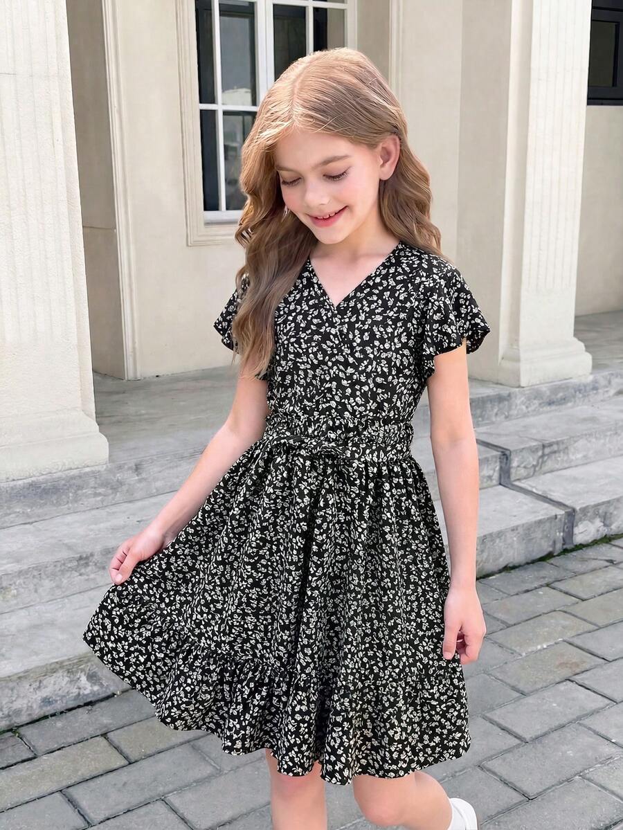 Tween girl wearing a black ditsy floral A-line short dress with V-neckline and flounce short sleeves.