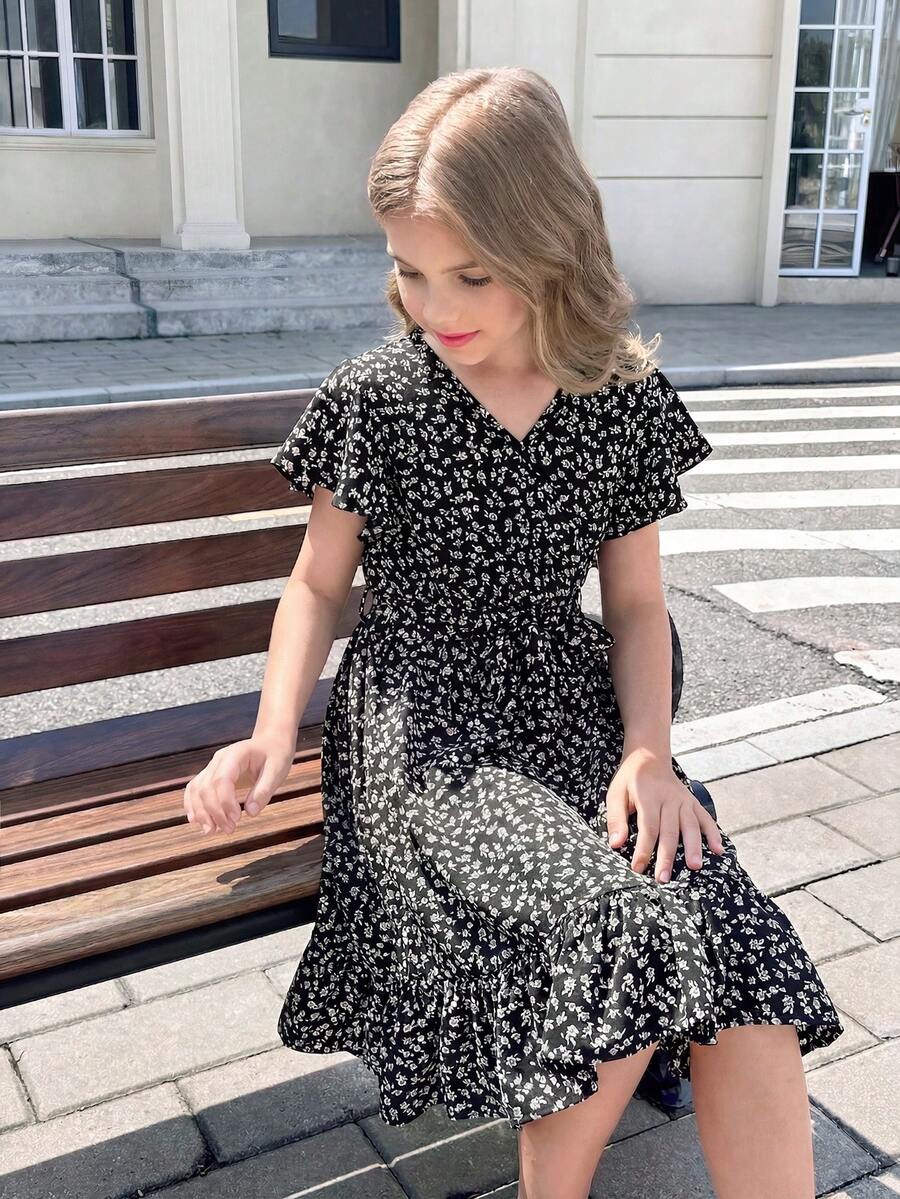 Tween girl wearing a black ditsy floral A-line short dress with V-neckline and flounce short sleeves.