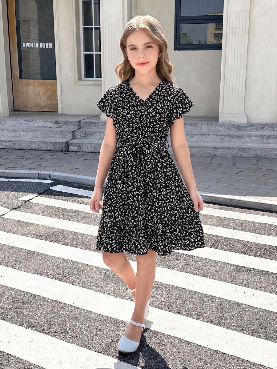 Tween girl wearing a black ditsy floral A-line short dress with V-neckline and flounce short sleeves.