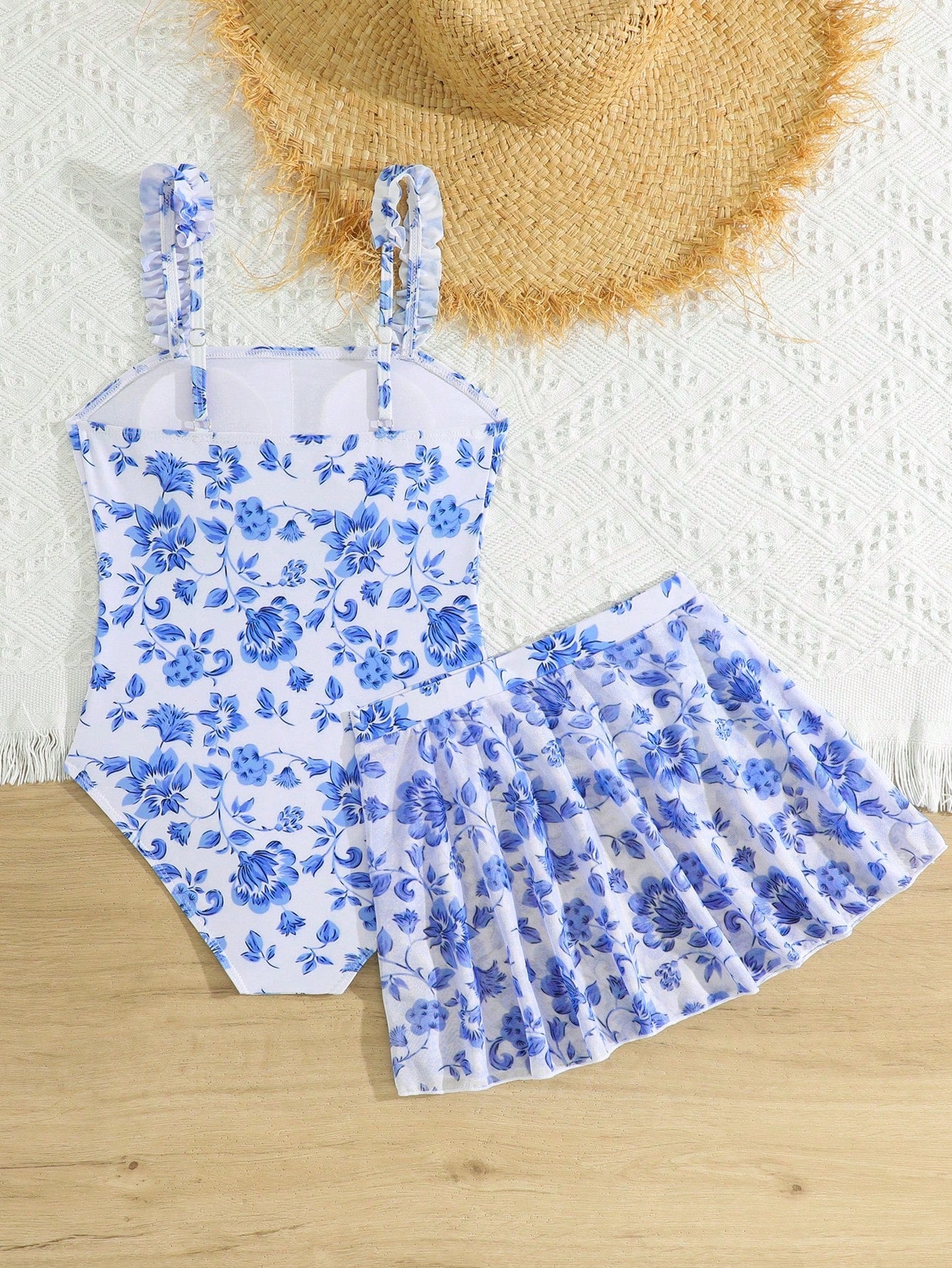 Blue tween girls one-piece swimsuit with tropical plant print, spaghetti straps, ruffle detail, and skirt-style mid-waist bottom for beach and pool wear.