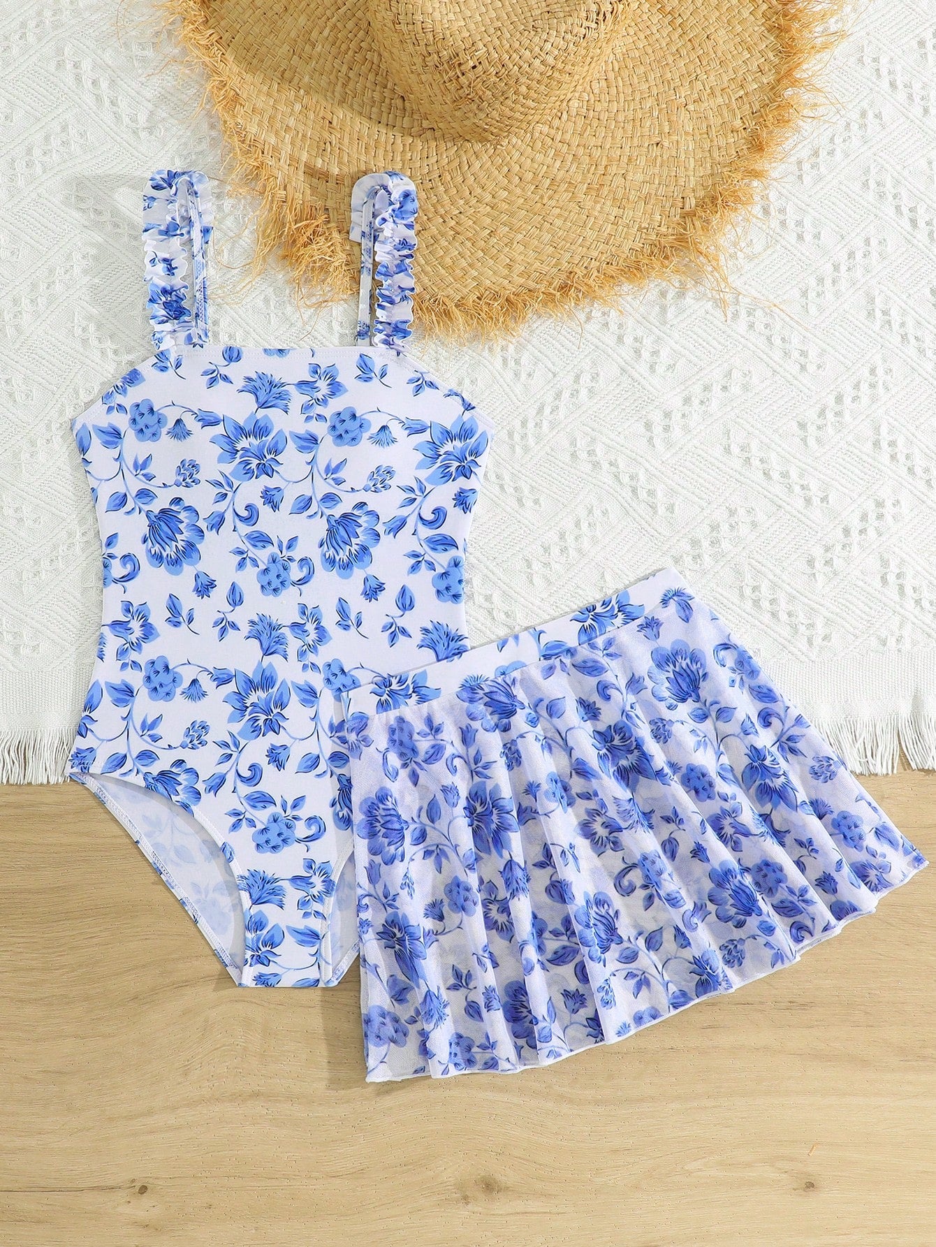 Blue tween girls one-piece swimsuit with tropical plant print, spaghetti straps, ruffle detail, and skirt-style mid-waist bottom for beach and pool wear.
