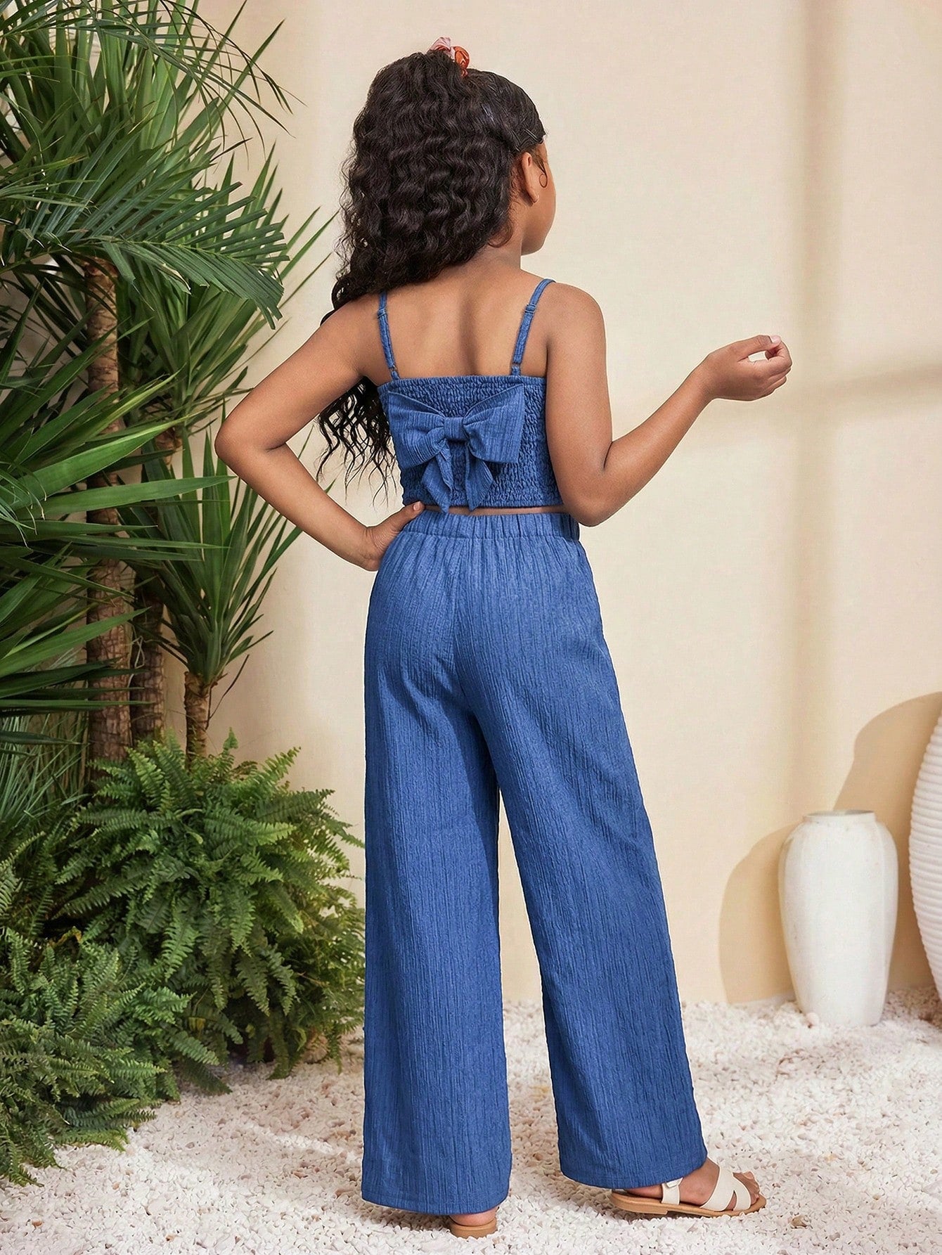 Tween girl wearing a black sleeveless spaghetti strap camisole top with 3D bow decor and matching leopard print wide leg long pants.