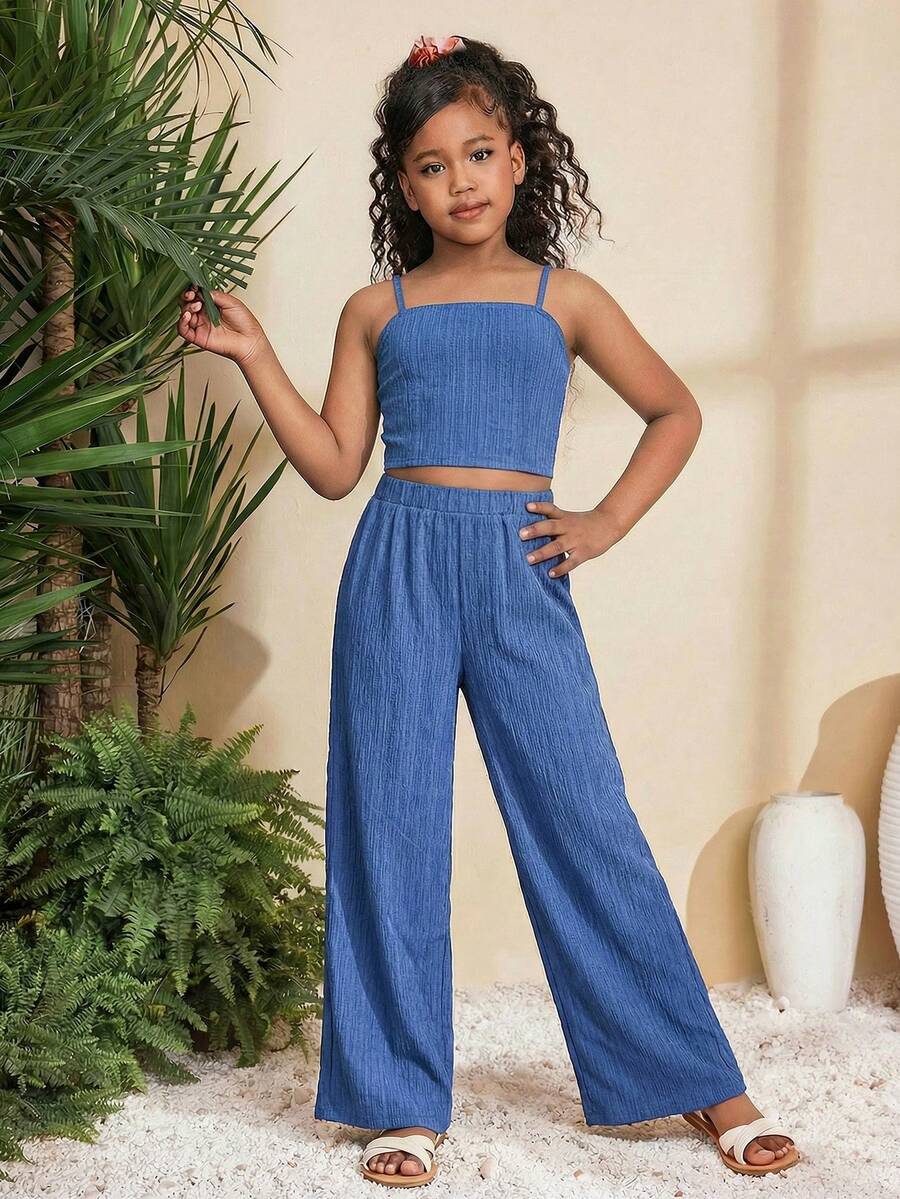 Tween girl wearing a black sleeveless spaghetti strap camisole top with 3D bow decor and matching leopard print wide leg long pants.
