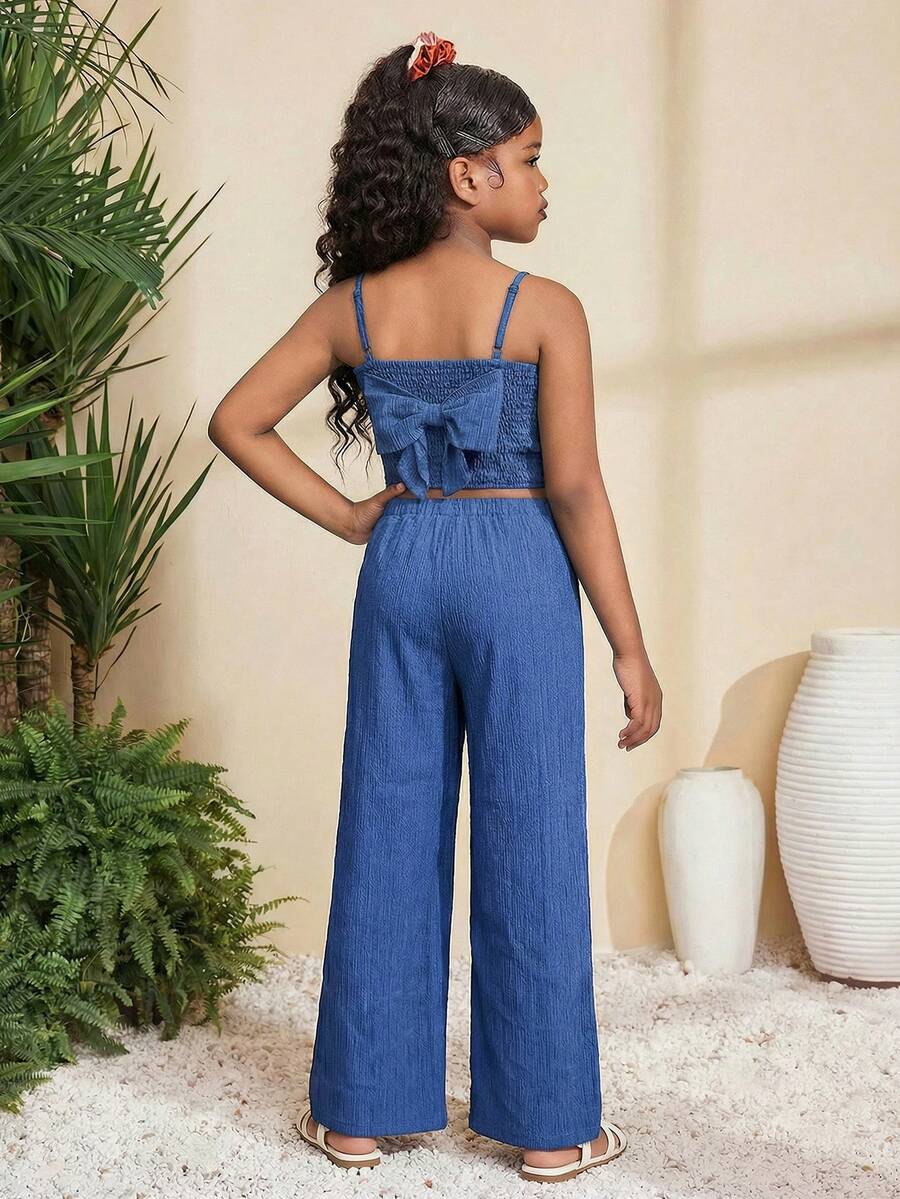 Tween girl wearing a black sleeveless spaghetti strap camisole top with 3D bow decor and matching leopard print wide leg long pants.
