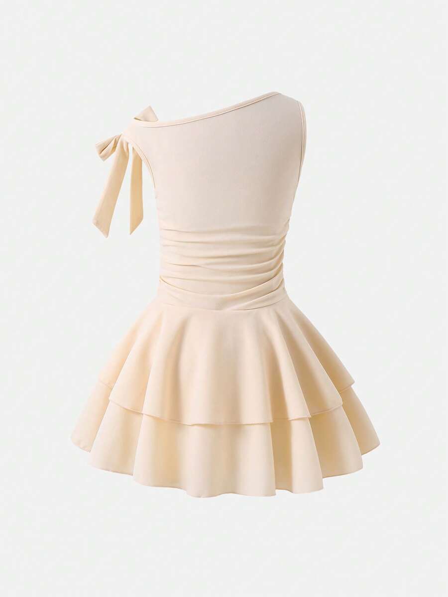 Tween girl wearing an apricot asymmetric skater dress with ruffle and applique details for party and formal occasions.