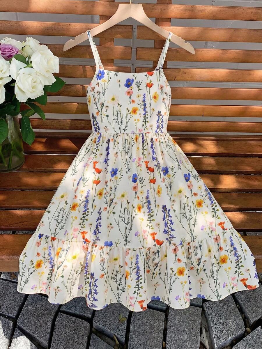 Tween girl wearing an apricot floral print sleeveless mini cami dress featuring spaghetti straps, a shirred high waist, flounce hem, and a bow back detail.