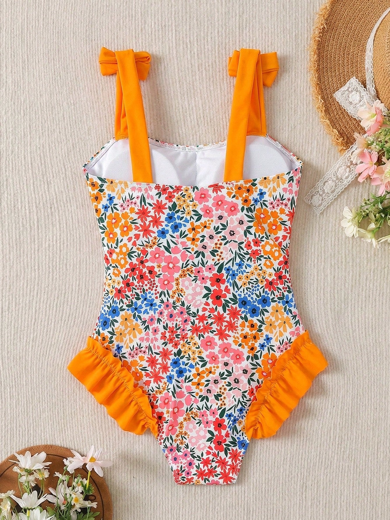 Girls' multicolor one-piece swimsuit with floral plant print, bow detail, asymmetrical ruffle accent, strap neckline, and lined body for beach vacations.